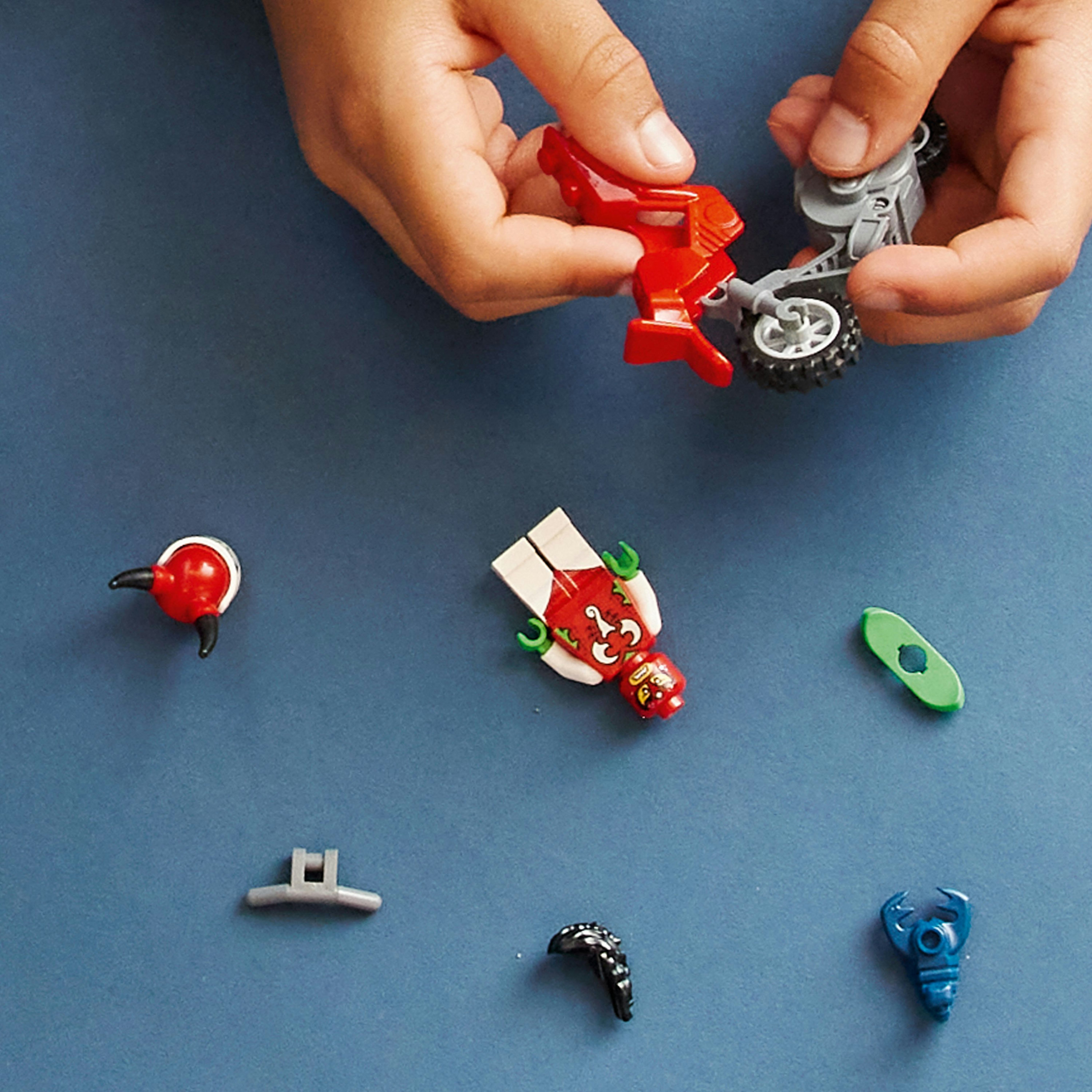 Manos construyen una moto LEGO. Piezas LEGO, incluyendo un motorista, están dispersas sobre una superficie azul.