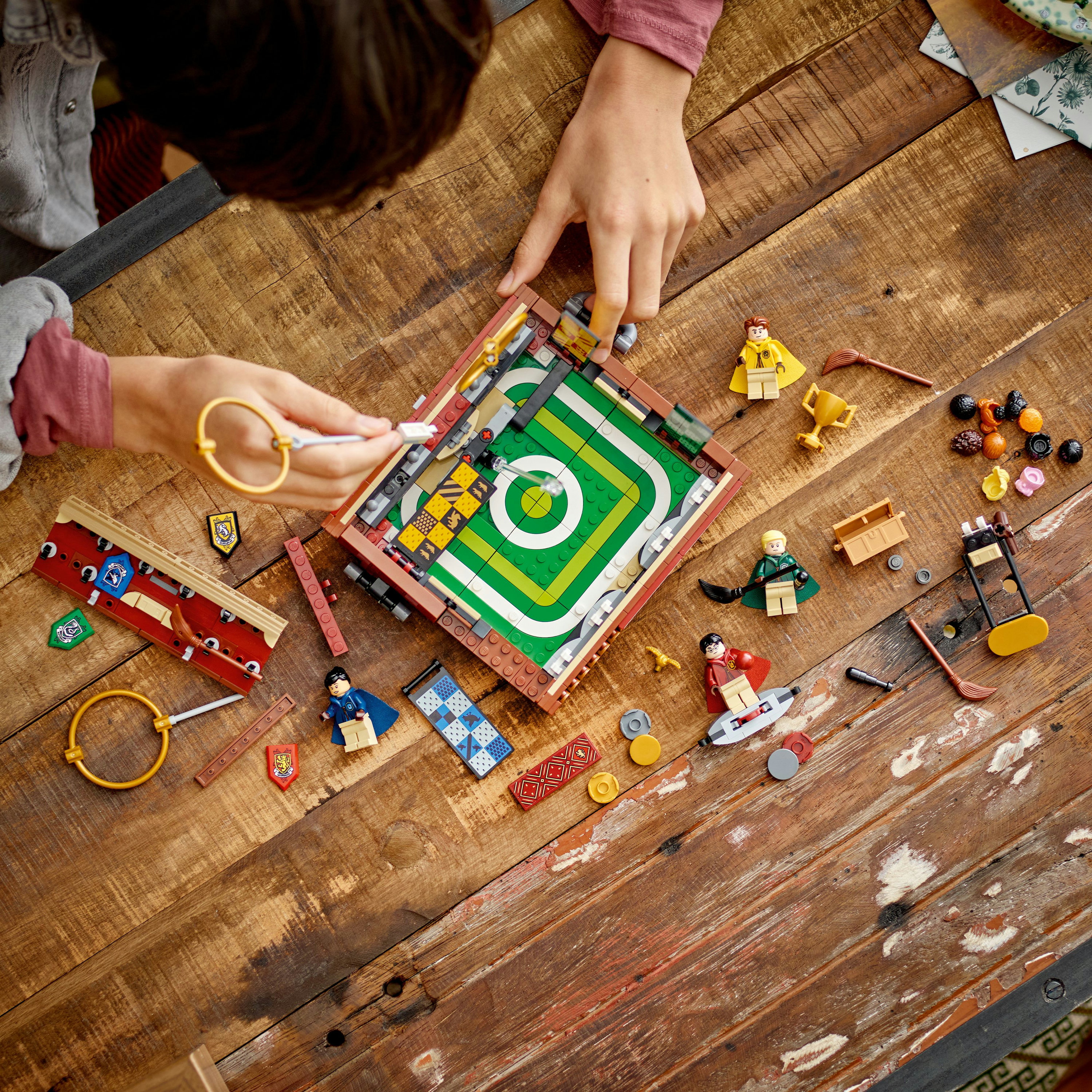 Ręce budują grę Lego na drewnianym stole. Są minifigurki, elementy gry i inne części Lego.