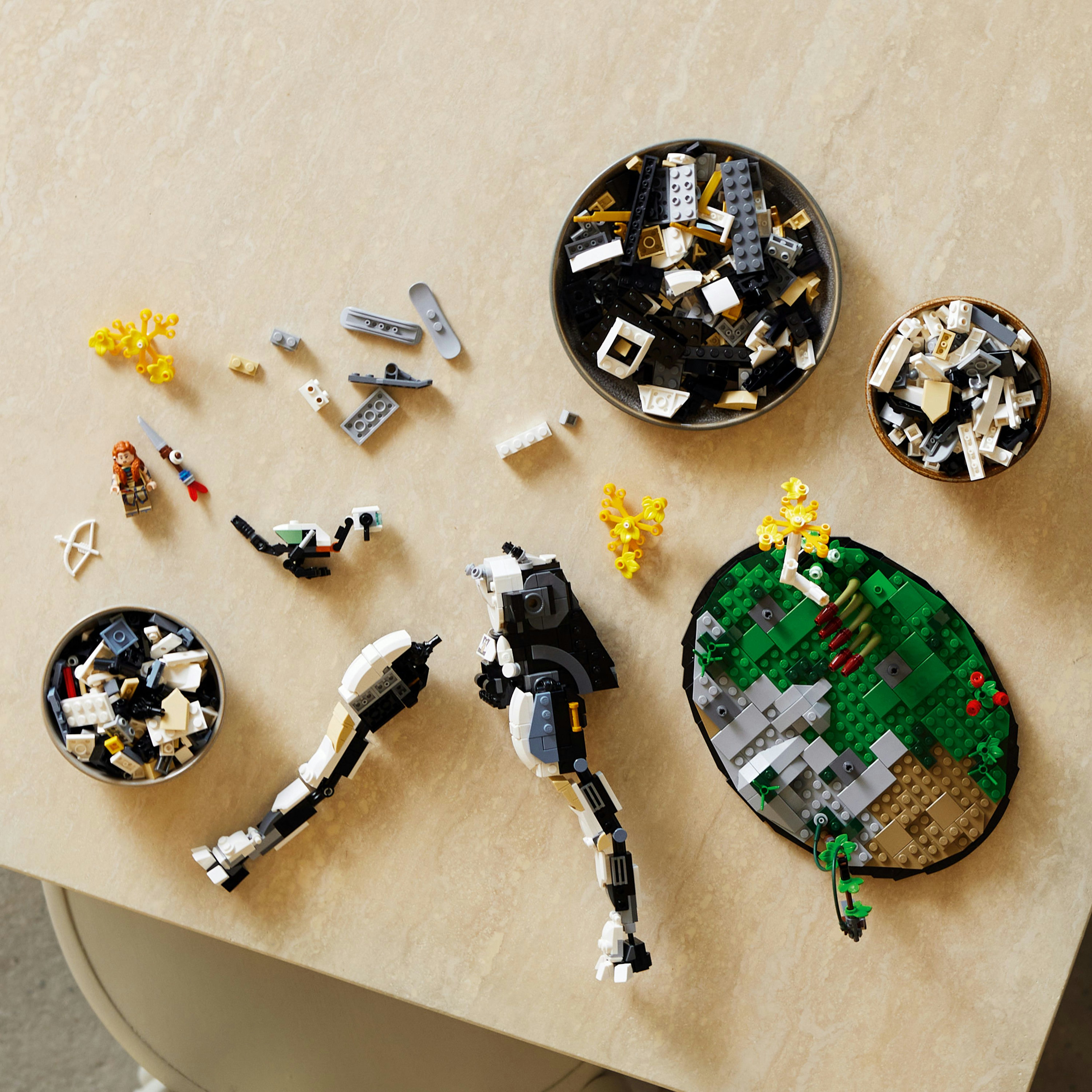 Lego-Teile, teilweise zusammengebaute Figuren und Schalen mit Lego-Steinen auf einem Tisch.