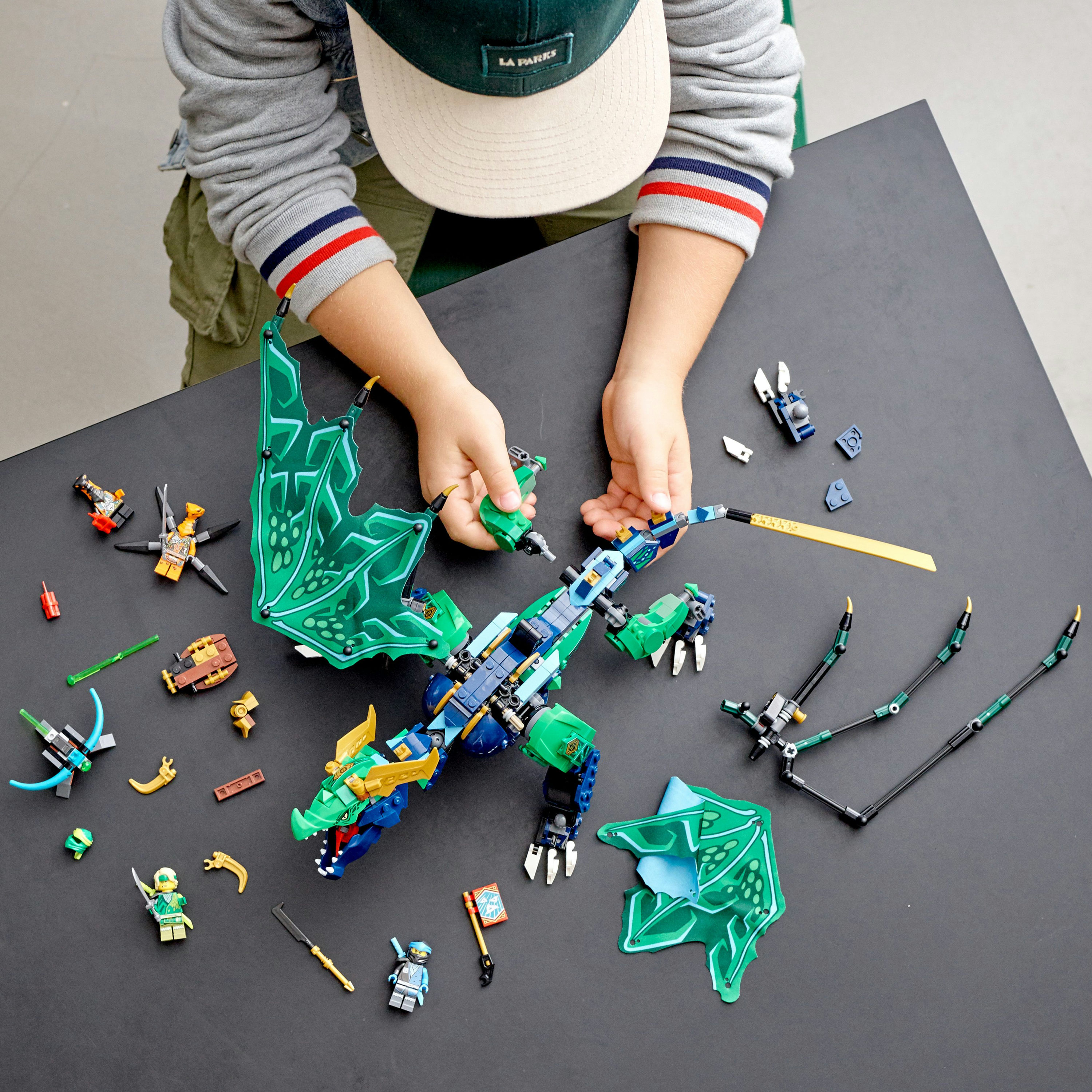 Un niño montando un dragón Lego. Muchas piezas de dragón están esparcidas sobre una superficie negra.