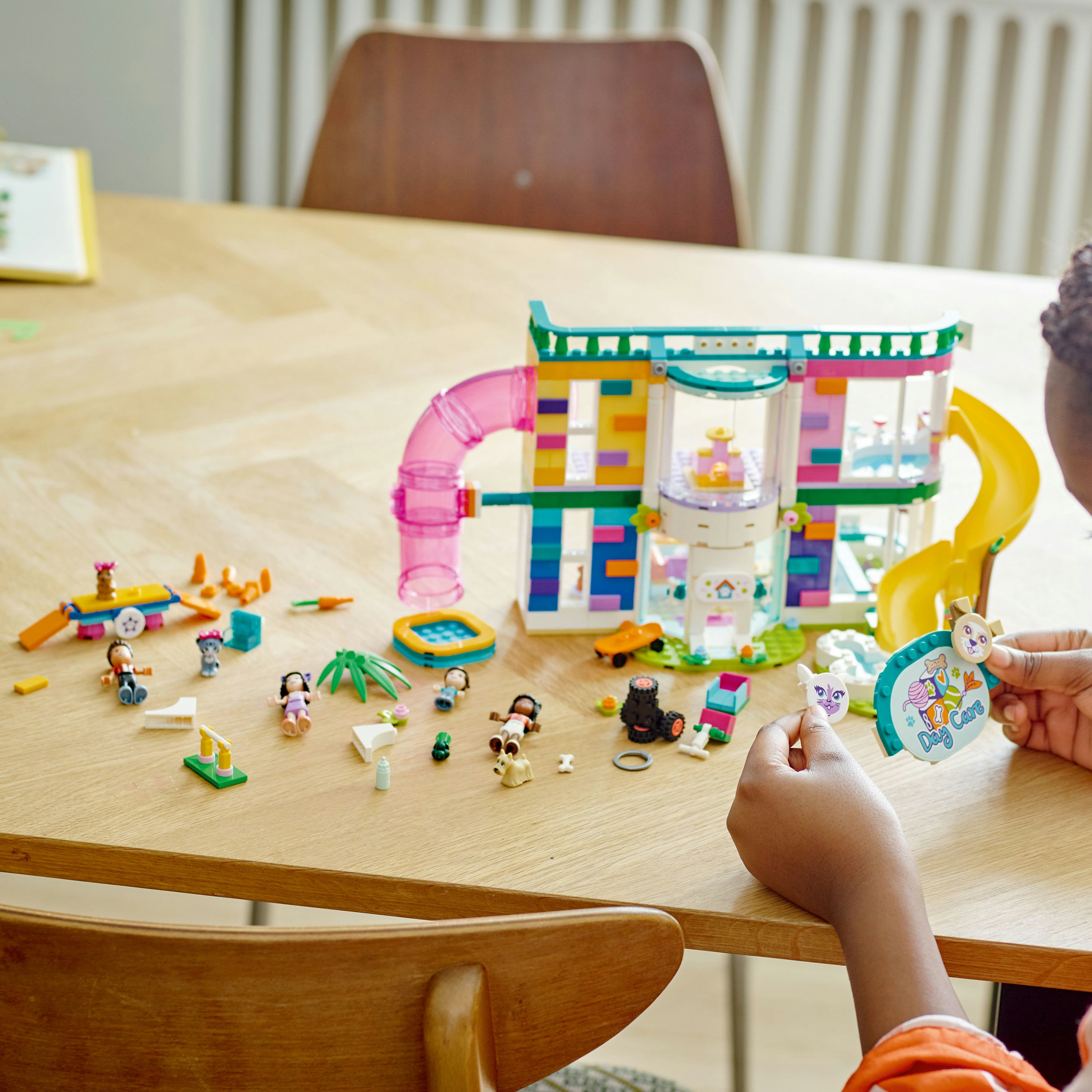 Dziecko bawi się zestawem Lego Friends. Zestaw przedstawia żłobek dla psów z akcesoriami.