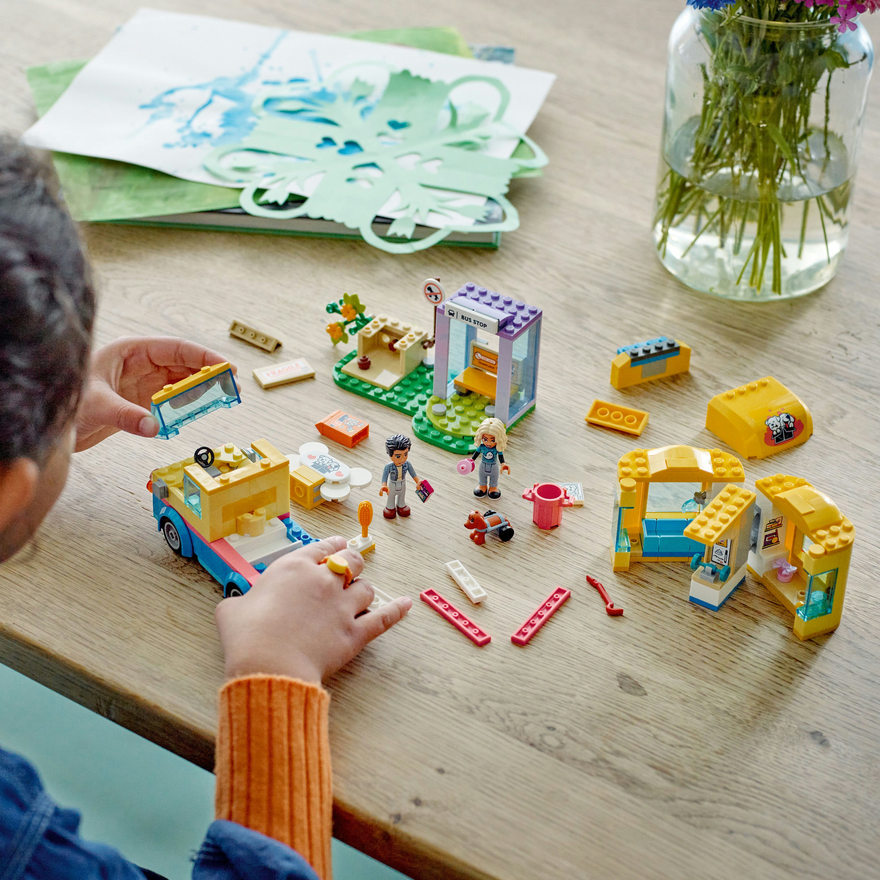 Un bambino gioca con set Lego, tra cui un'auto, un negozio e delle figure, su un tavolo di legno.