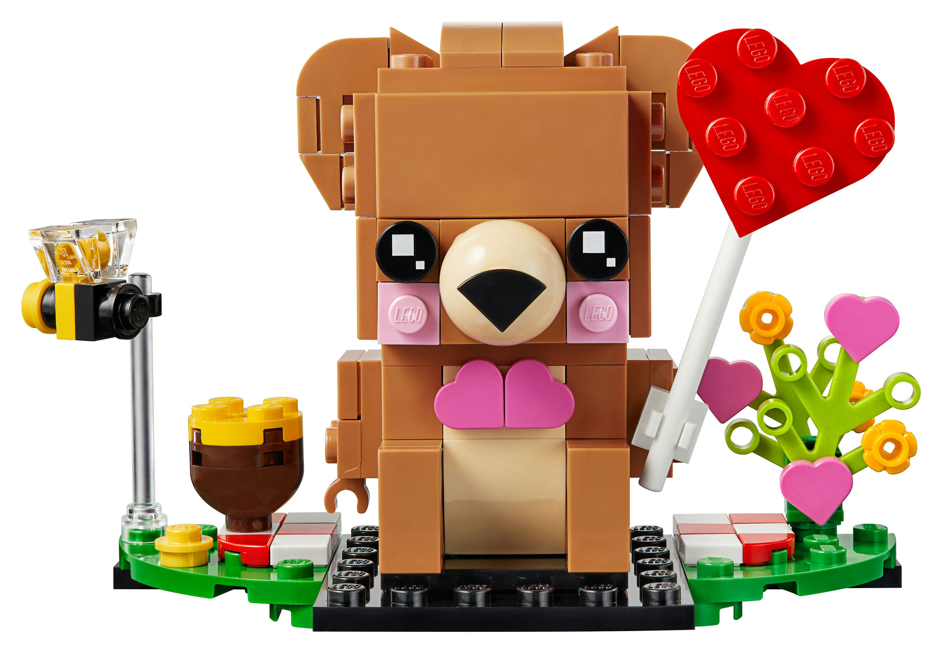 Lego set featuring a bear holding a heart-shaped balloon, flowers, and a bee with camera.
