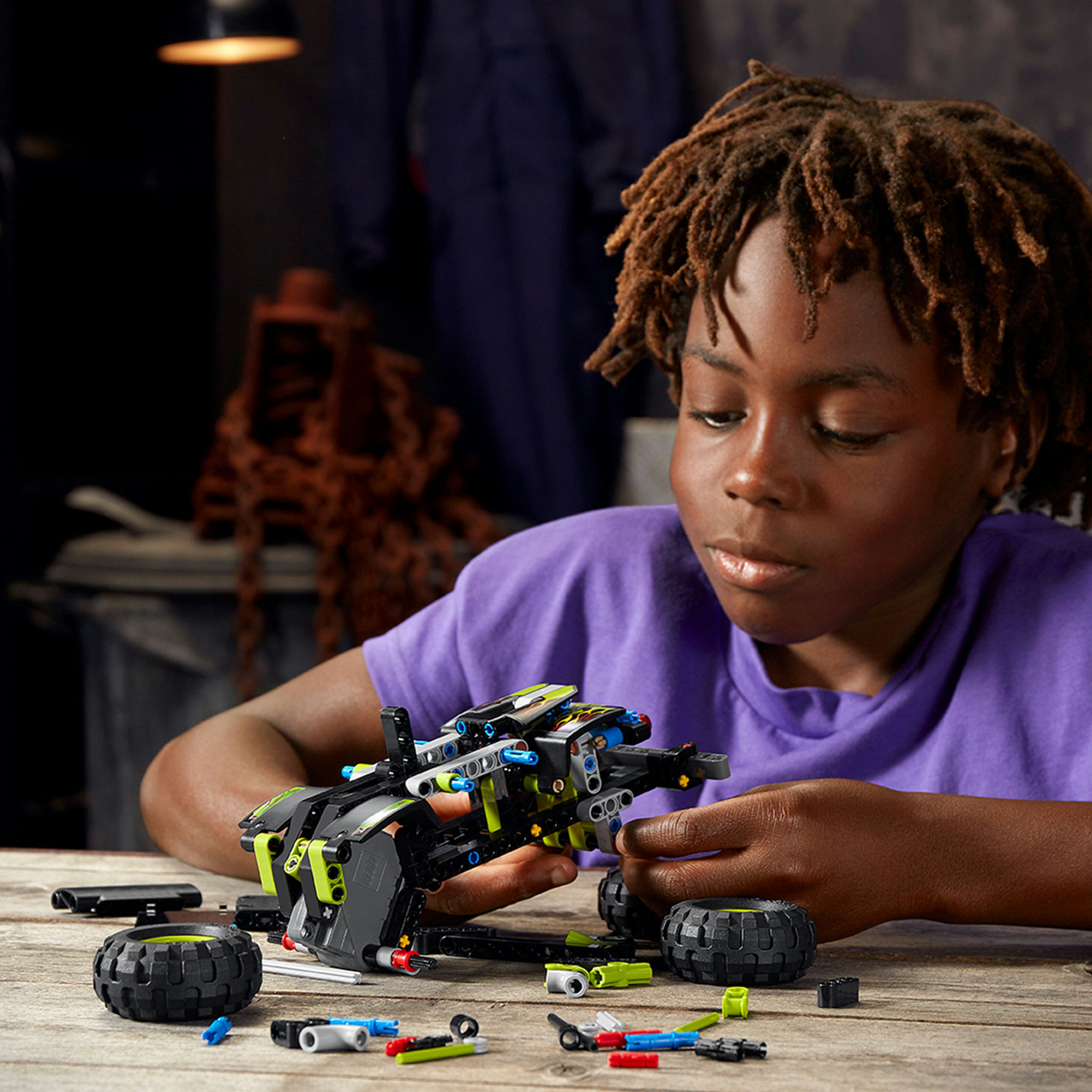 Bir çocuk siyah bir LEGO Technic aracı inşa ediyor. Aracın bazı yeşil unsurları var.