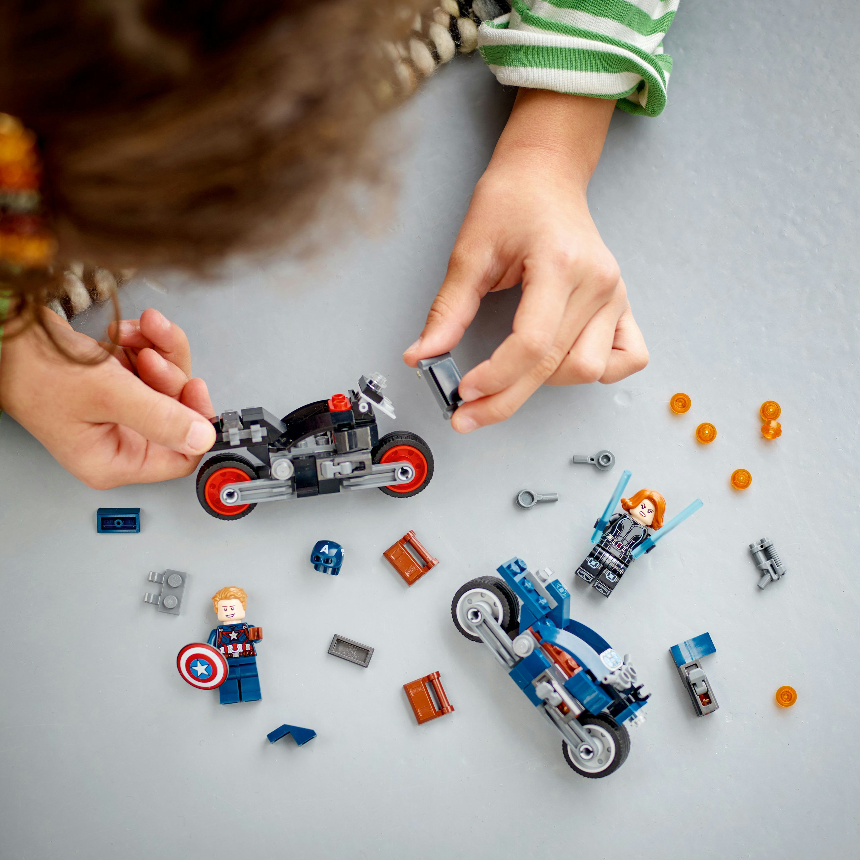 Çocuğun elleri, Lego Marvel setini topluyor. Kaptan Amerika ve Kara Dul figürleri ve motosikletler dahil.