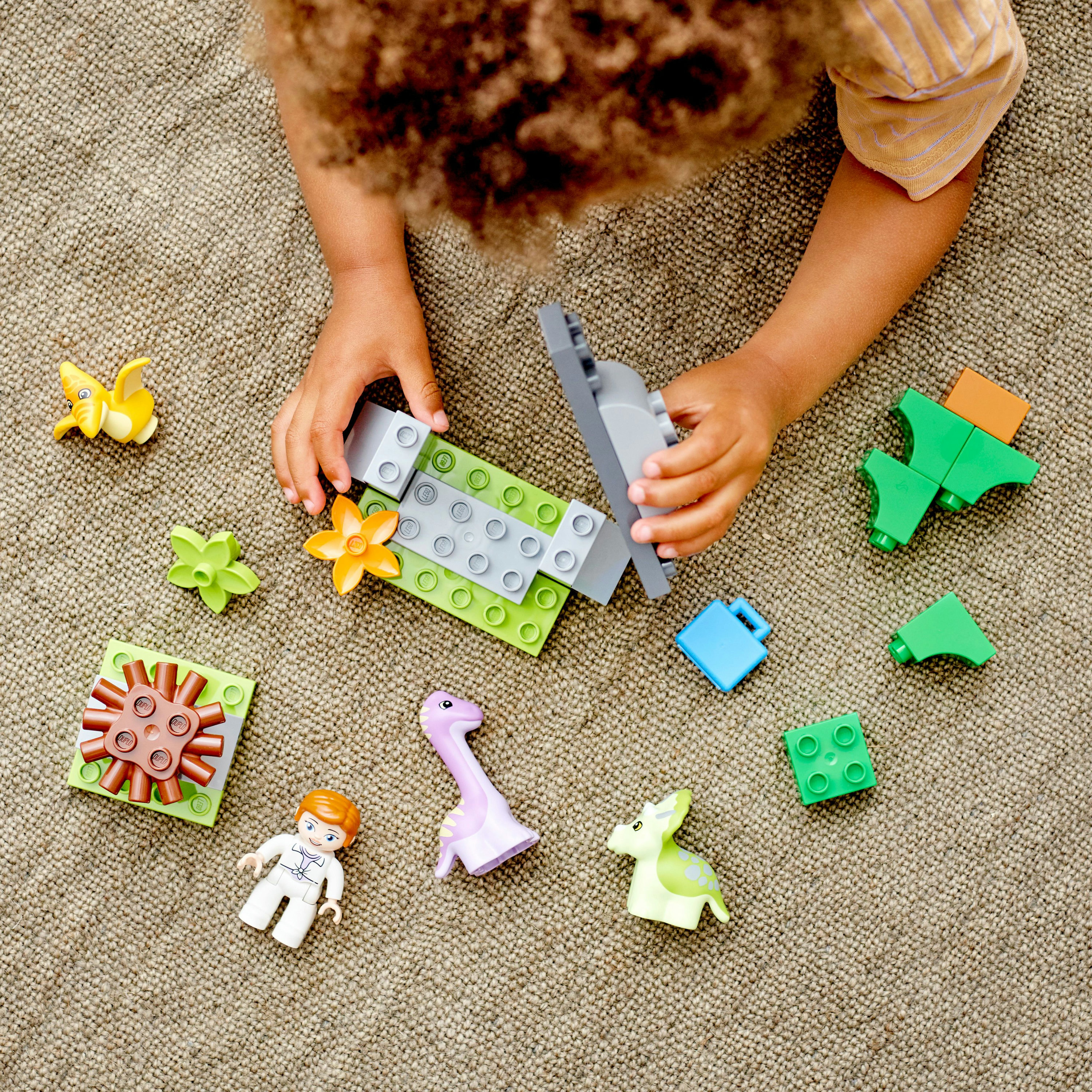 Kinderhände spielen mit Duplo-Steinen, darunter Dinosaurier und Blumen.