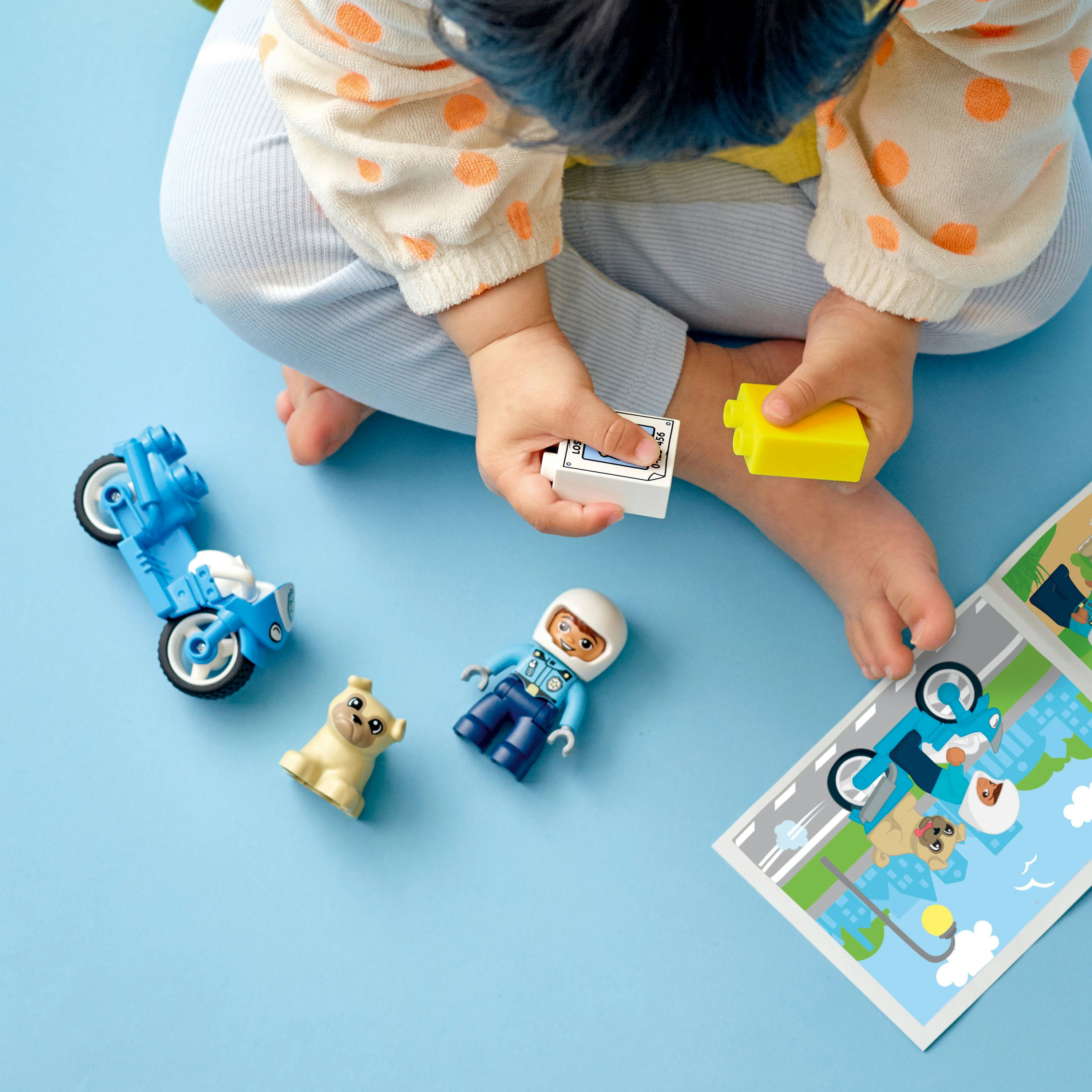 Een kind speelt met Lego Duplo. Er is een motor, een hond en een figuur.