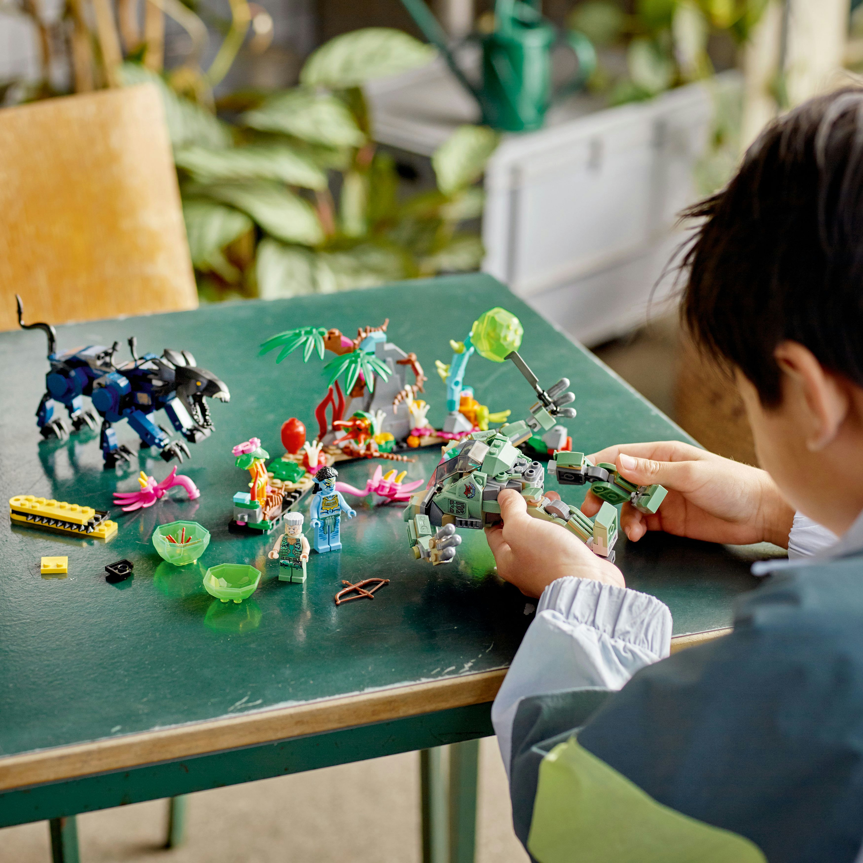 Un niño construyendo un juego de LEGO con varias criaturas y accesorios en una mesa verde, mostrando el proceso de construcción.