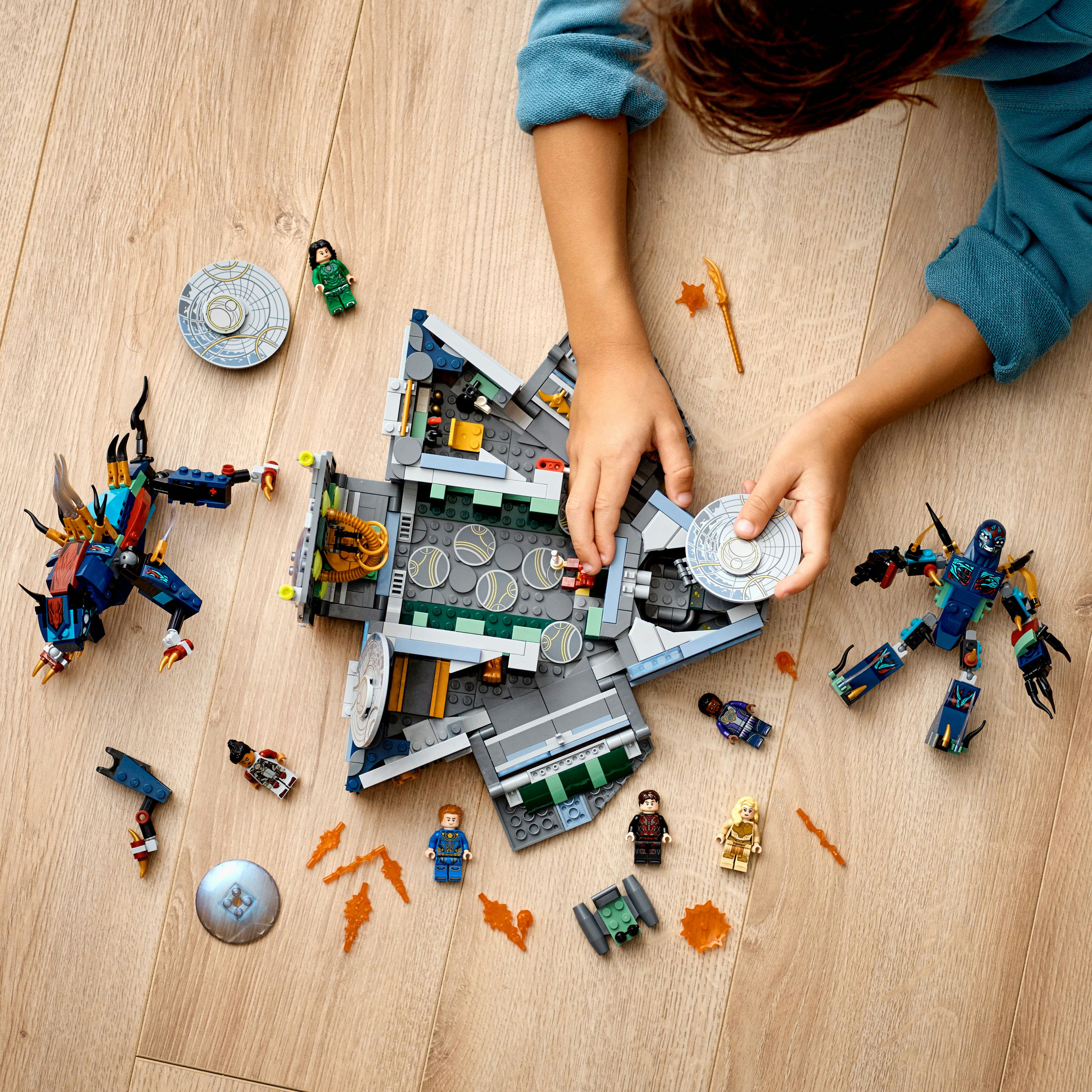 Kind spielt mit LEGO-Set. Ein großes Raumschiff ist von Minifiguren und kleinen LEGO-Teilen umgeben.
