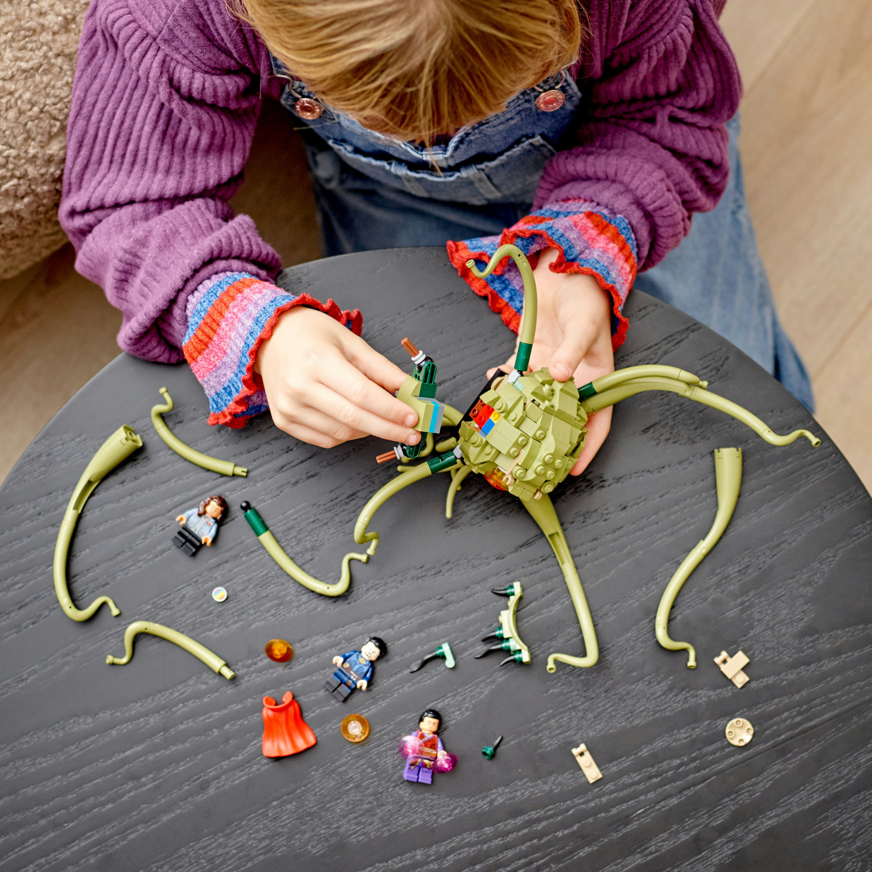 Ein Kind baut ein LEGO-Set mit grünen, tentakelartigen Strukturen und Minifiguren auf einem Tisch.
