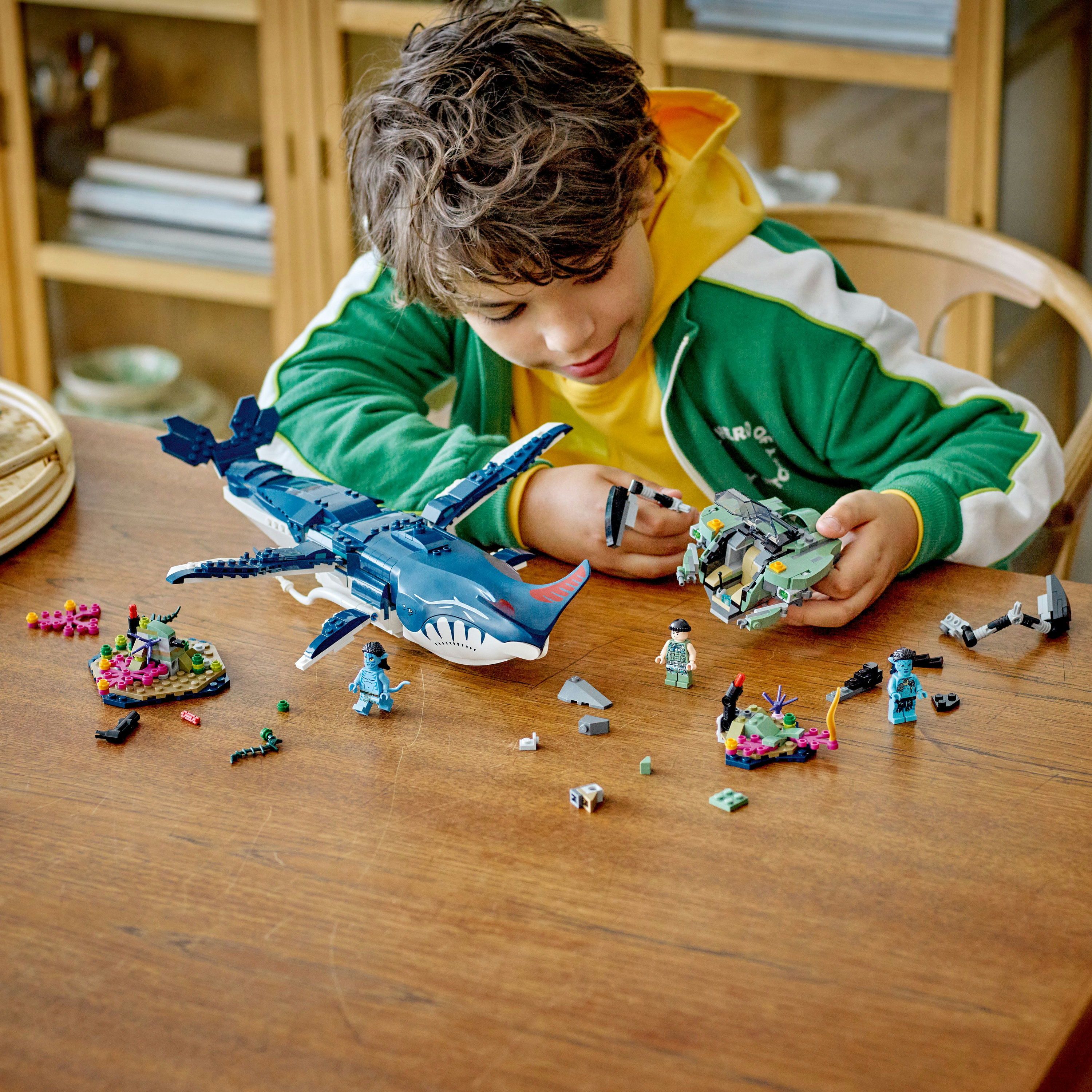 Un ragazzo gioca con set LEGO Avatar, tra cui uno squalo e un'astronave, su un tavolo di legno.