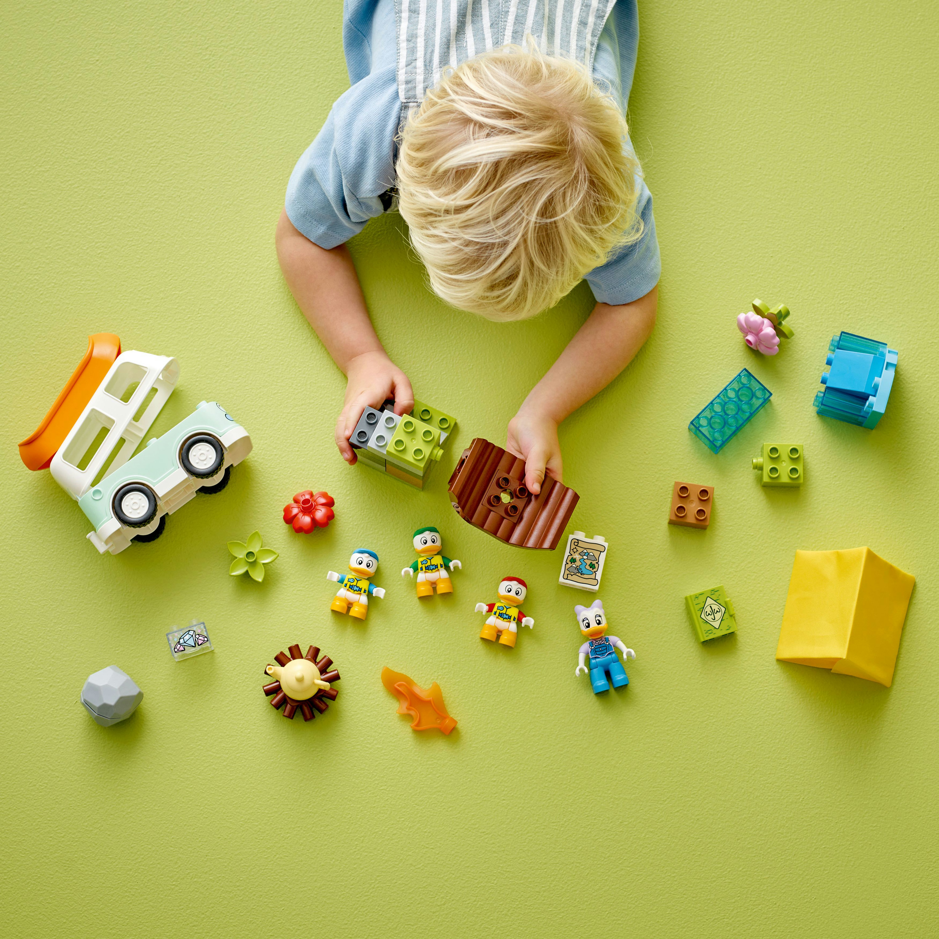 Ein Kind spielt mit Lego Duplo-Steinen. Verstreute Steine, Figuren und ein Spielzeug-LKW auf Grün.