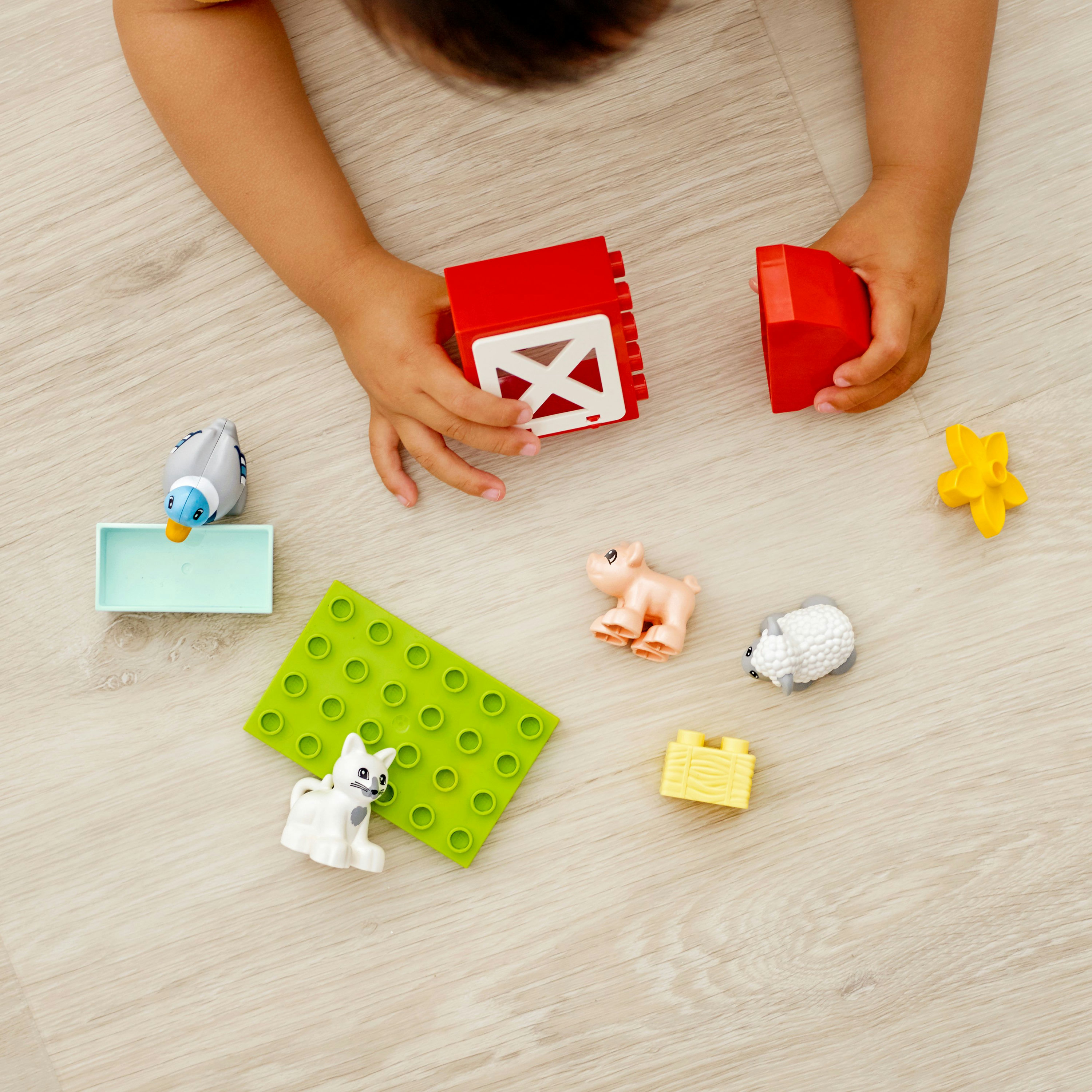 Kinderhände, die mit Lego Duplo-Bauernhof-Set-Teilen auf einer hellen Holzoberfläche interagieren.