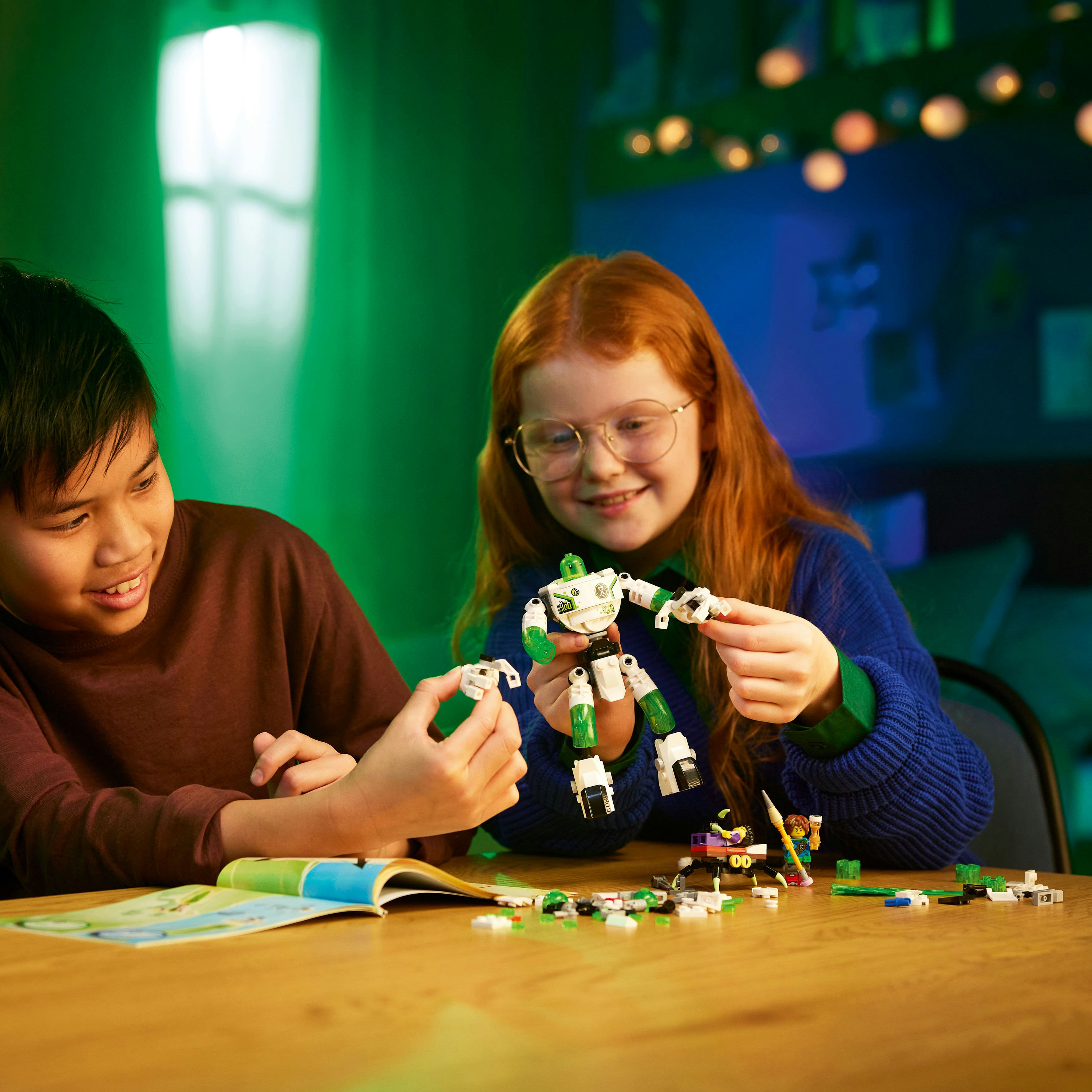 Due bambini costruiscono un robot giocattolo su un tavolo di legno. La scena è interna, con illuminazione verde e blu.