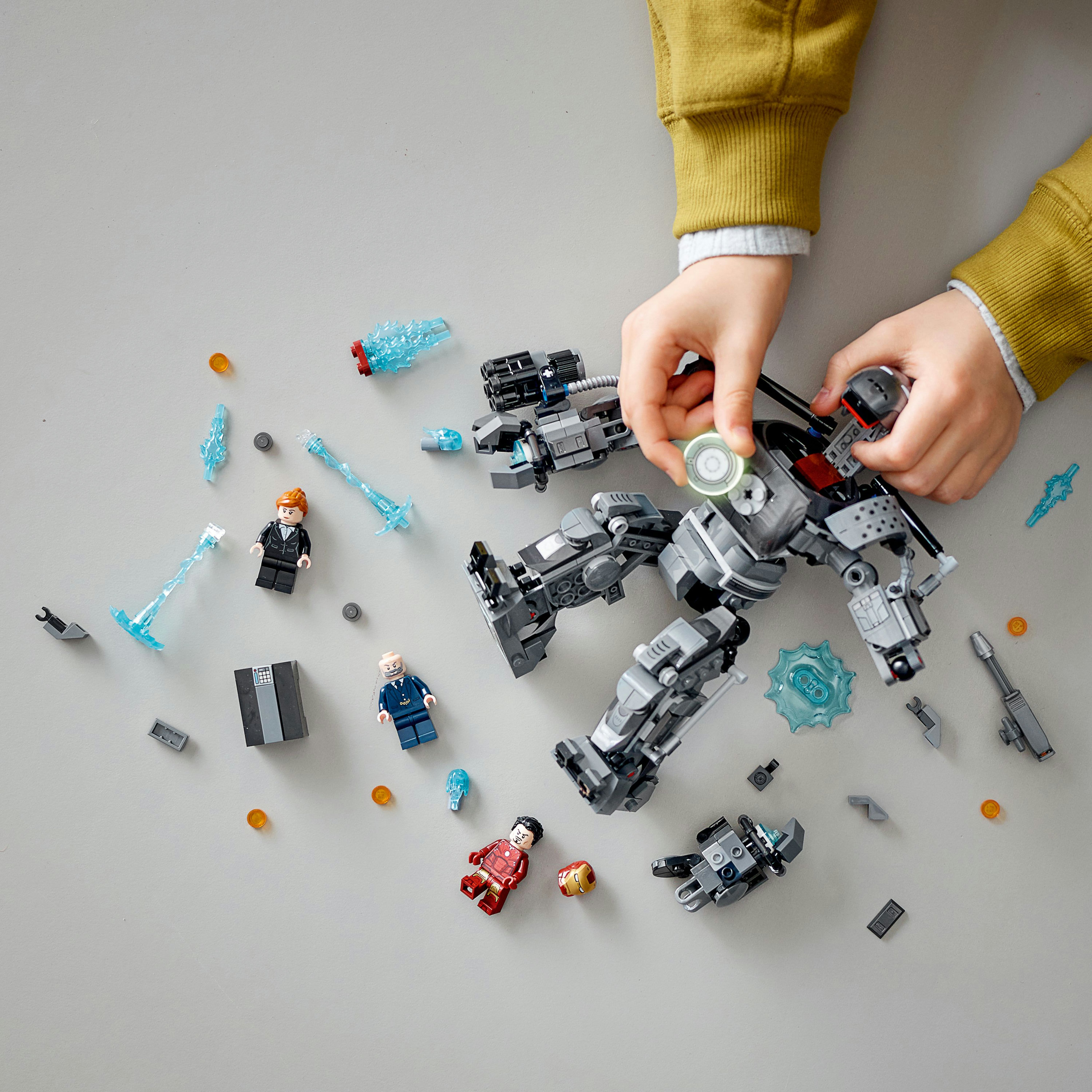 Mani di bambino che interagiscono con un mech LEGO grigio. Altre figure e pezzi sparsi.