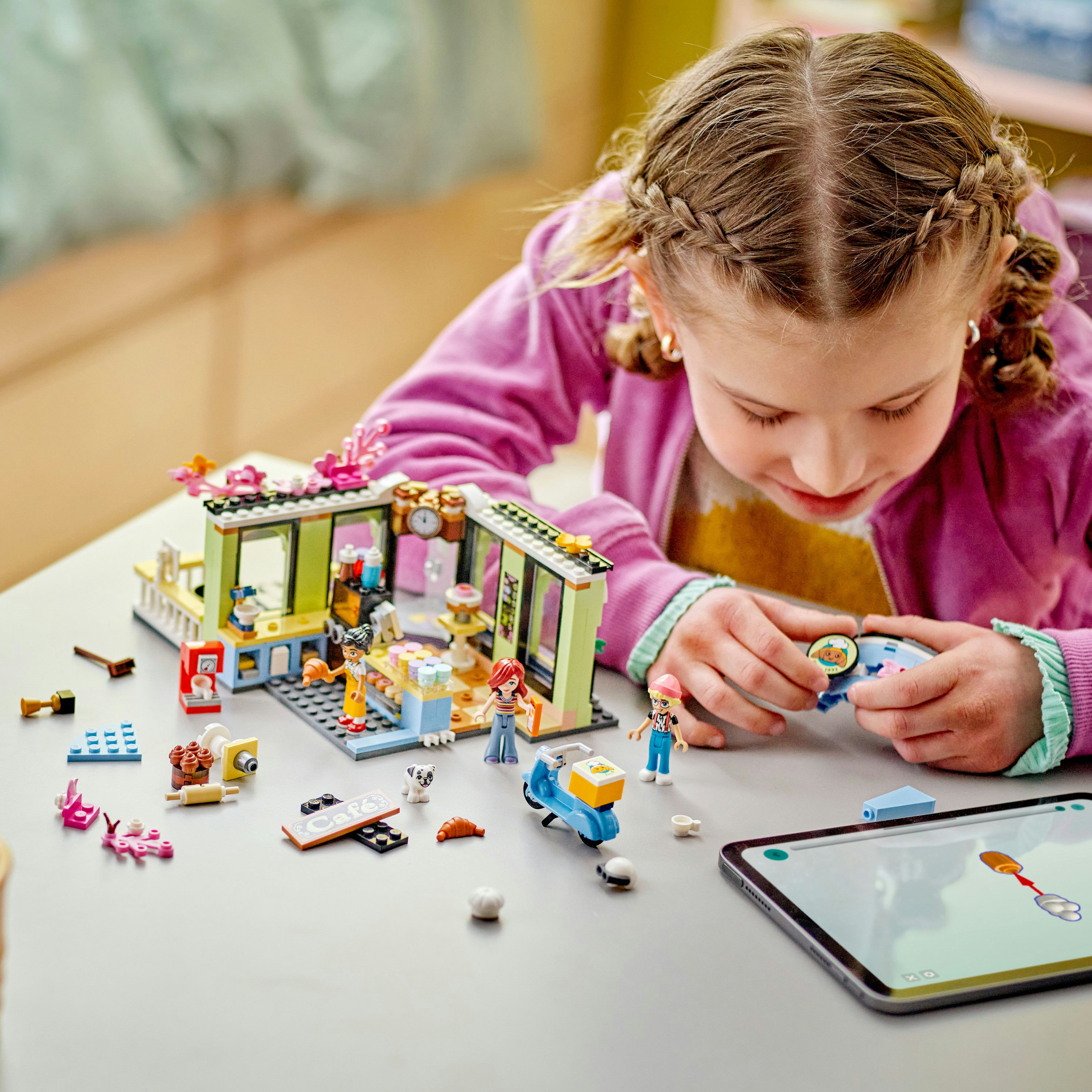 Dziewczynka bawi się zestawem LEGO Friends, składając sklep z różnymi mini-figurkami i akcesoriami.