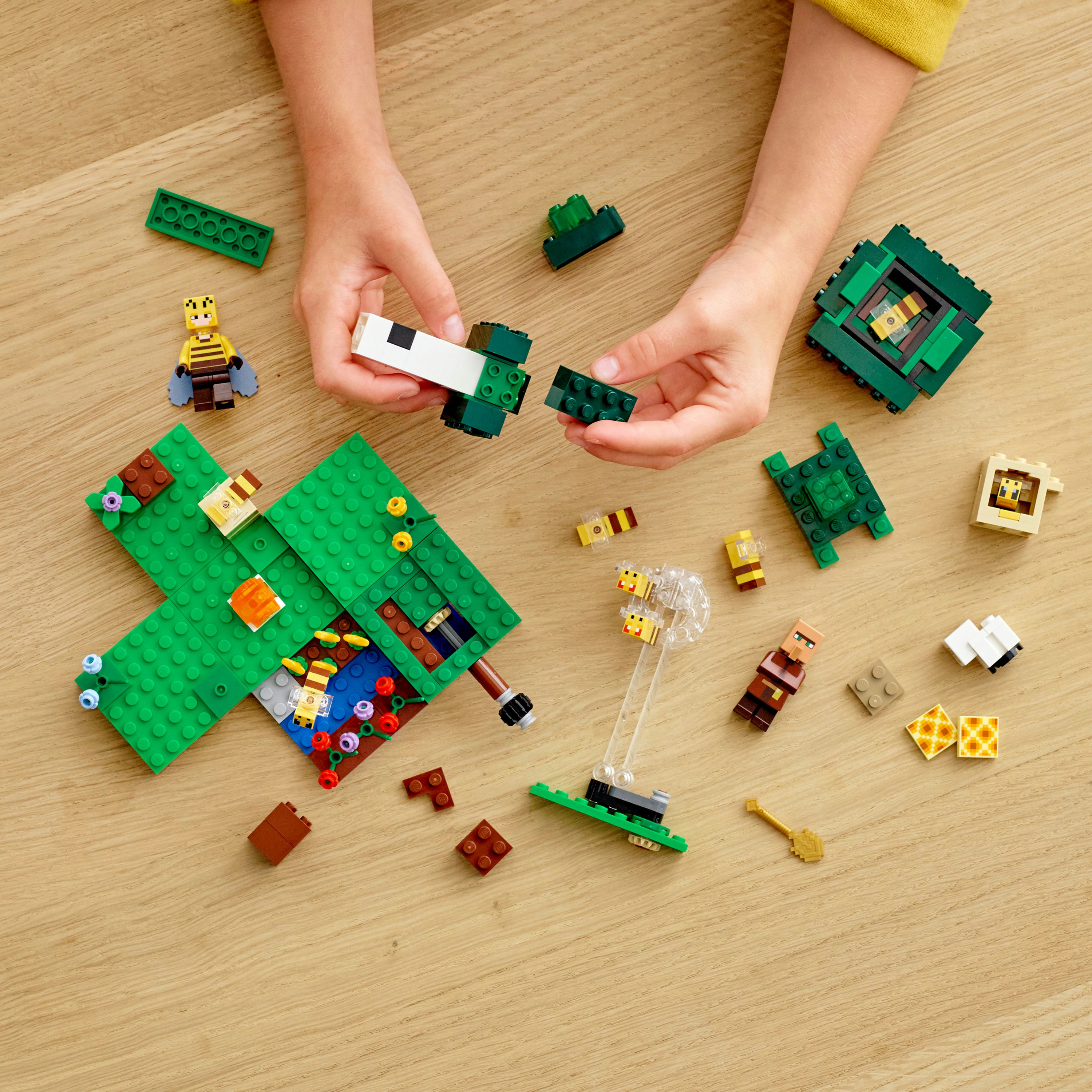 Hände montieren ein LEGO Minecraft-Set auf einer Holzoberfläche mit verschiedenen Steinen und Figuren.