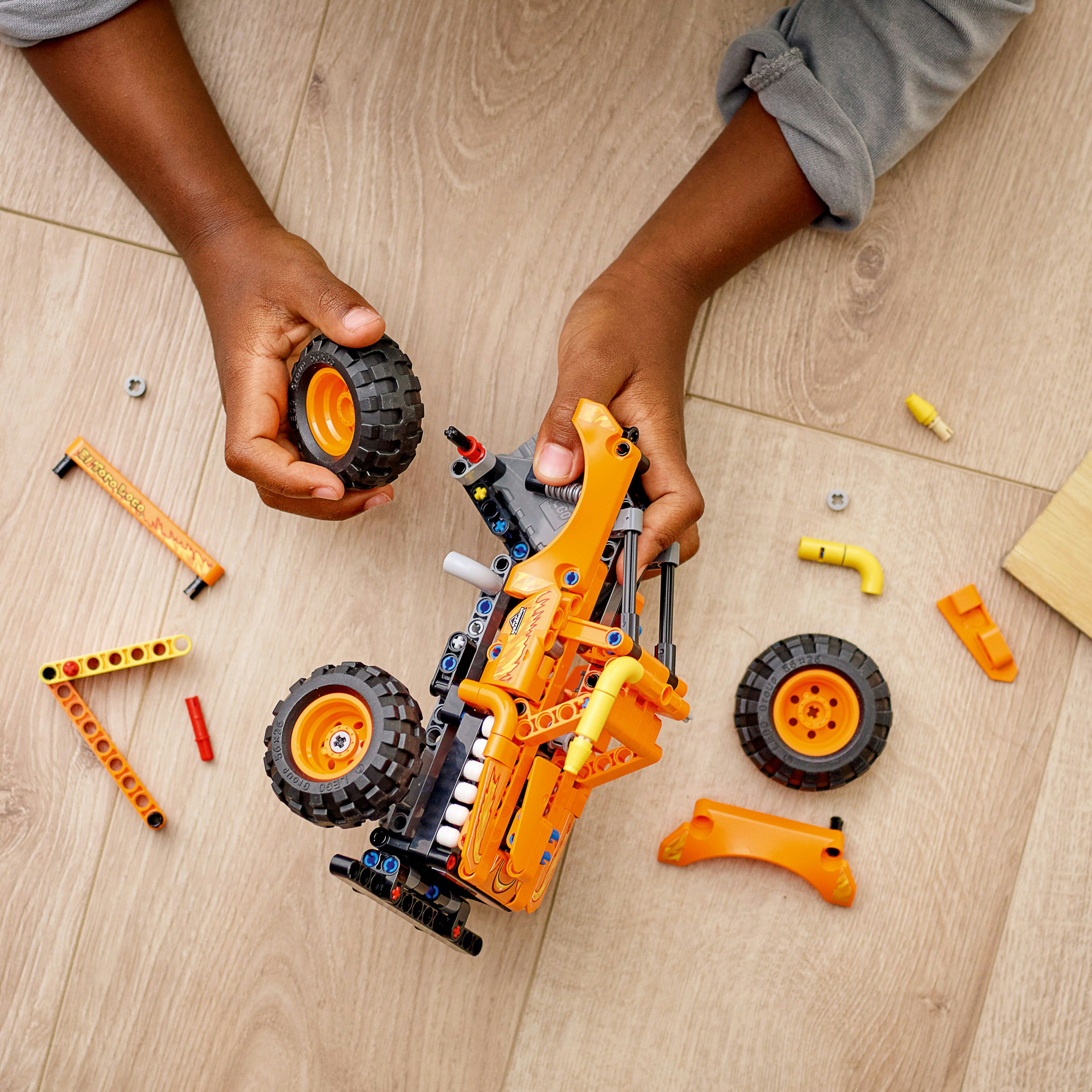 Le mani di un bambino che assemblano un veicolo LEGO Technic con parti arancioni e nere.