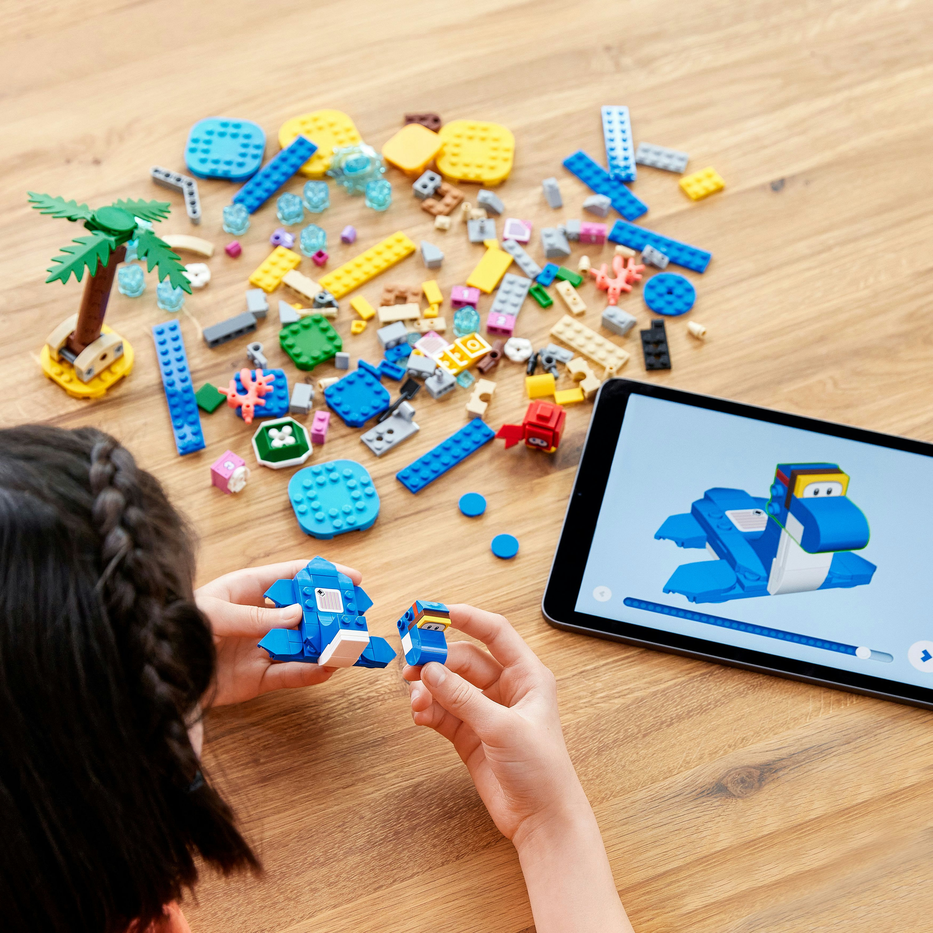 Ein Kind baut ein Lego-Modell mit verstreuten Steinen und einem Tablet mit Anweisungen.