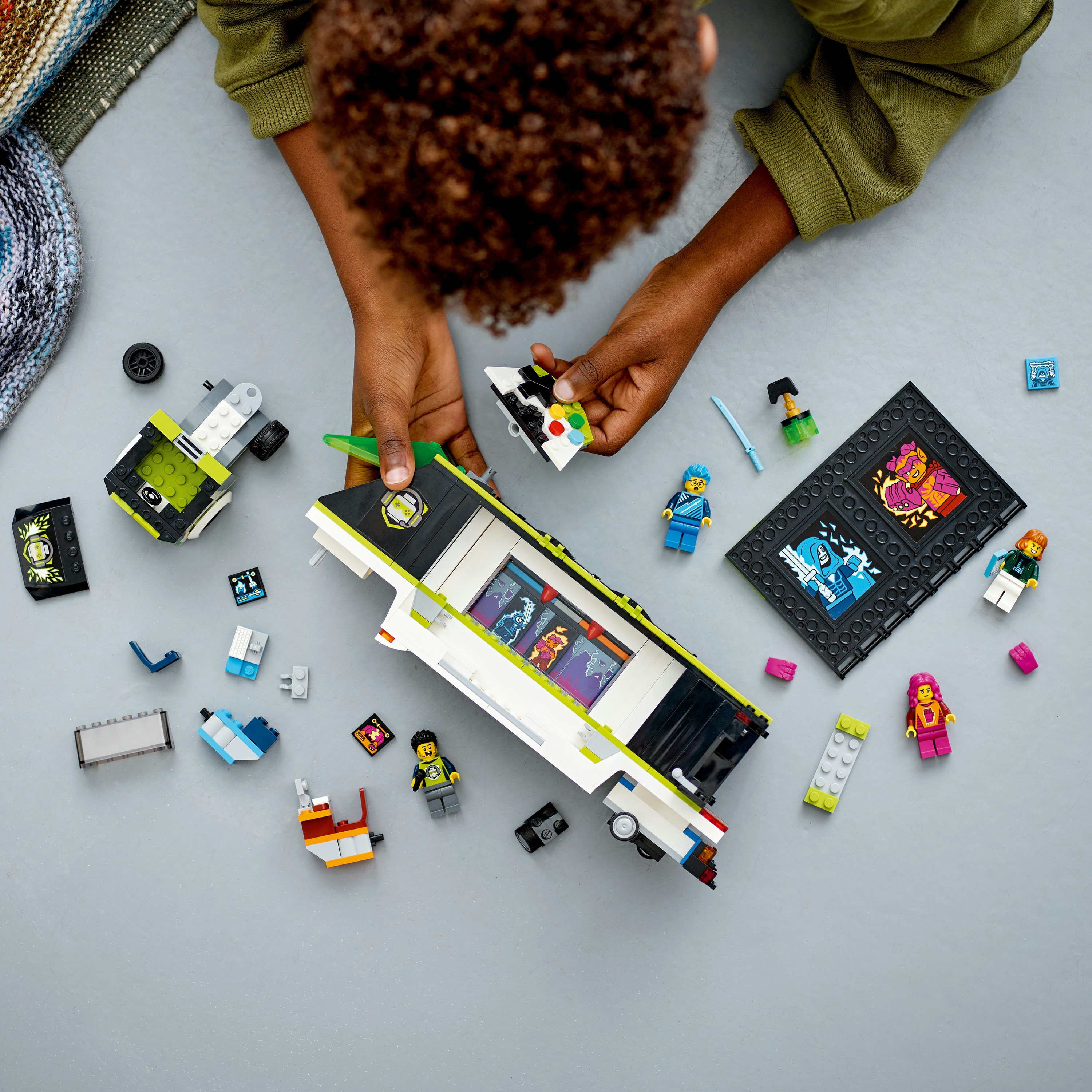 Manos de niño ensamblando piezas de Lego, con figuras Lego y un vehículo Lego.