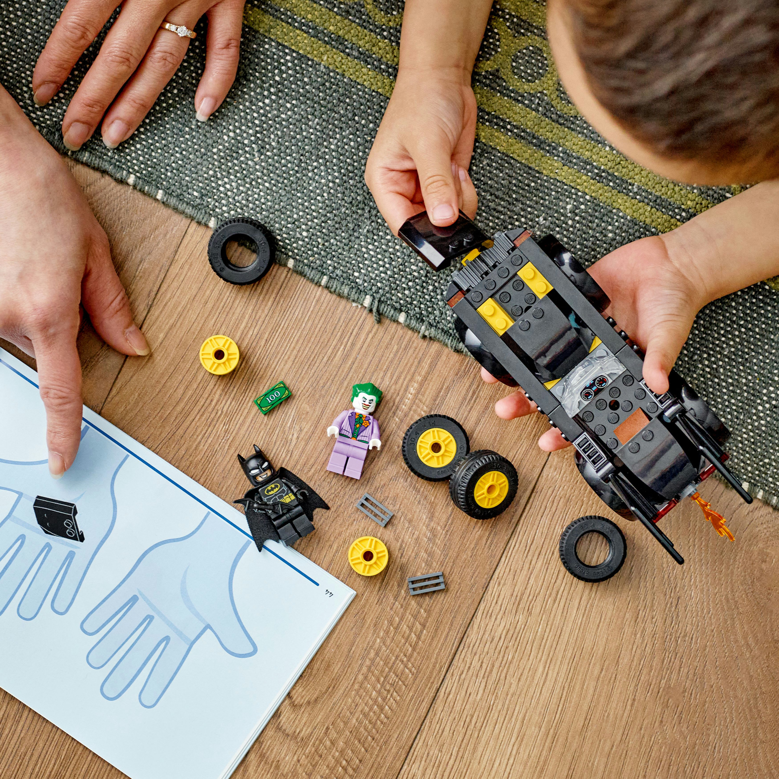 Ein Kind und ein Erwachsener bauen ein Lego Batman Auto Set. Minifiguren und Teile sind zu sehen.