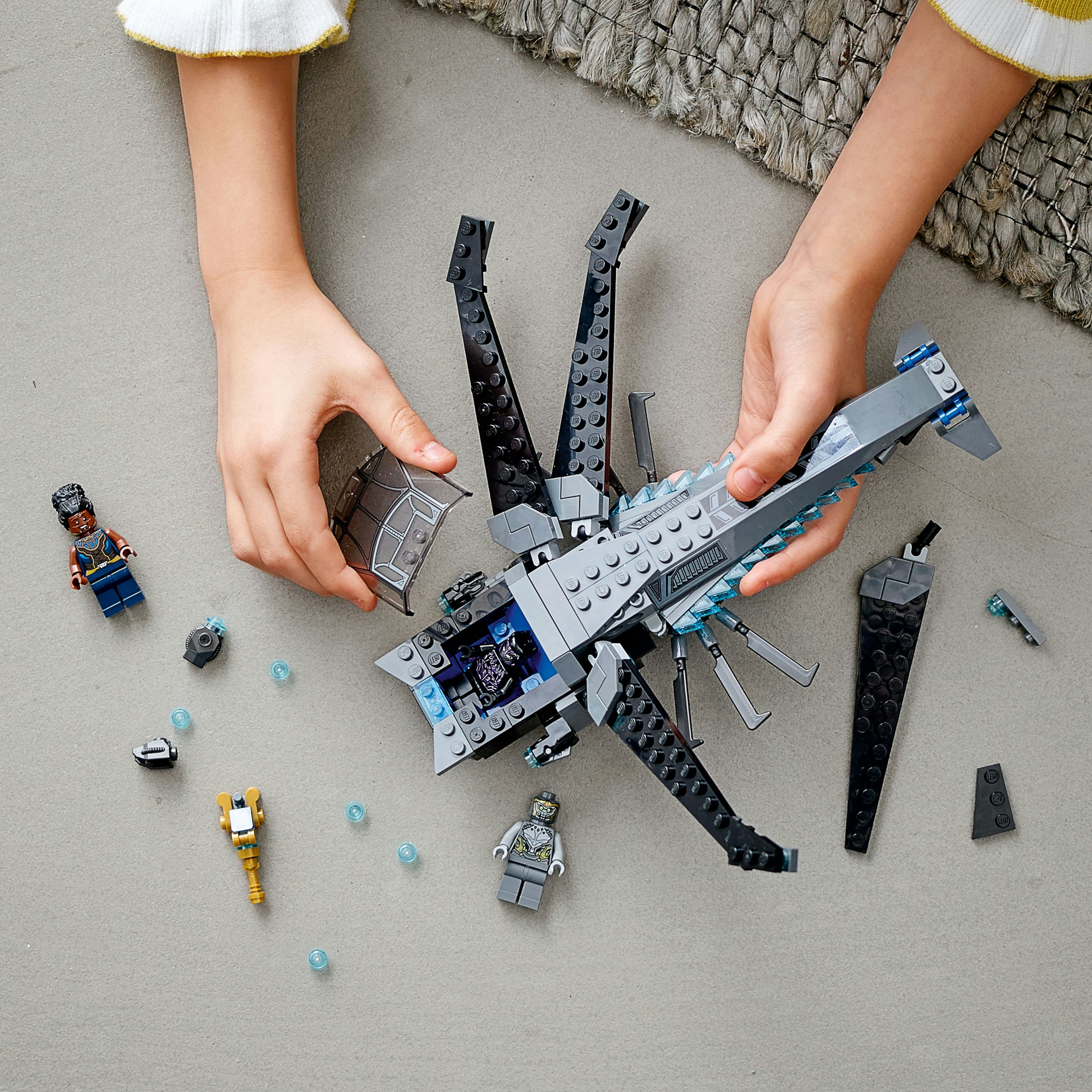 Hände, die Lego-Set zusammensetzen: Ein Lego-Set mit Figuren und Teilen auf grauer Oberfläche, Draufsicht.
