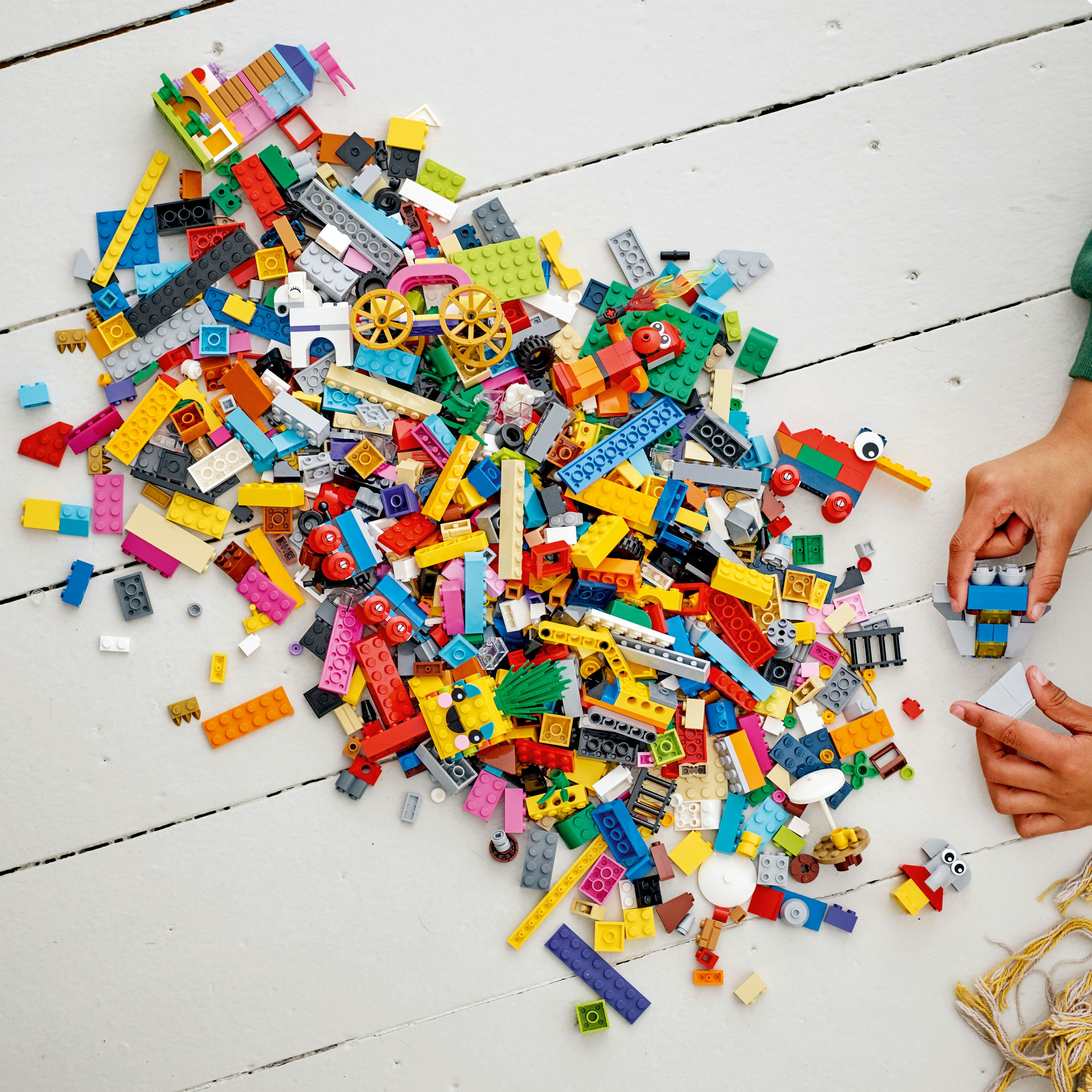 Beyaz bir yüzeyde dağınık bir yığın Lego tuğlası. Bir çocuk, renkli tuğlalarla bir yapı inşa ediyor.
