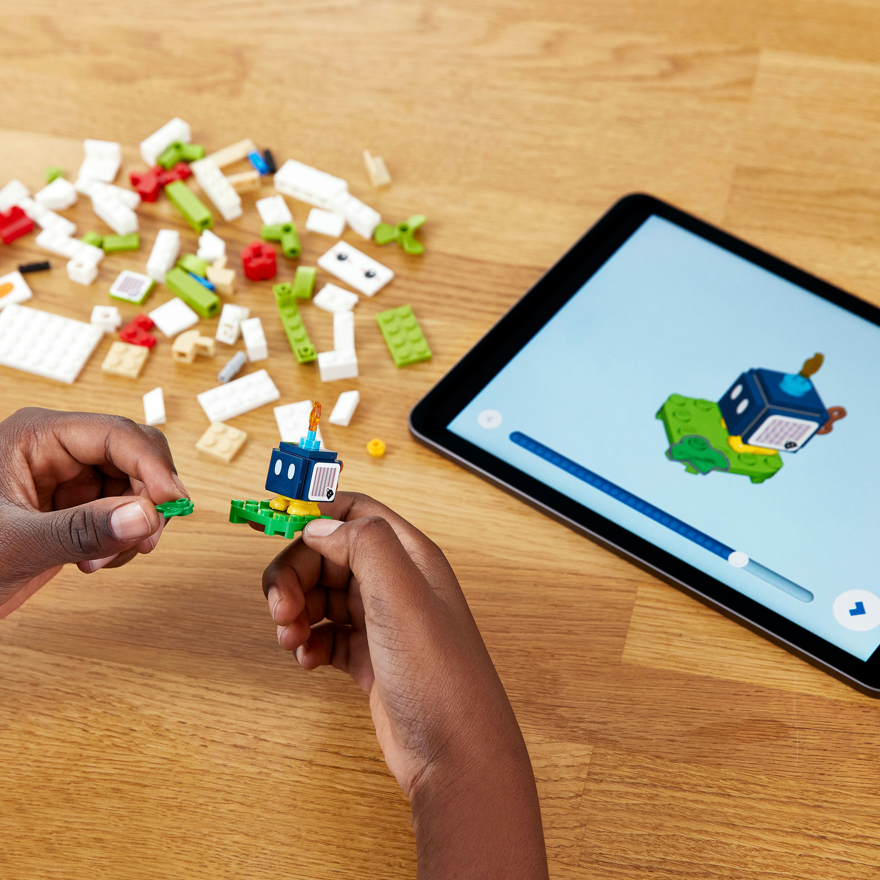 Hände bauen mit Legosteinen und einem Tablet. Das Tablet zeigt eine Lego-Bauanleitung.