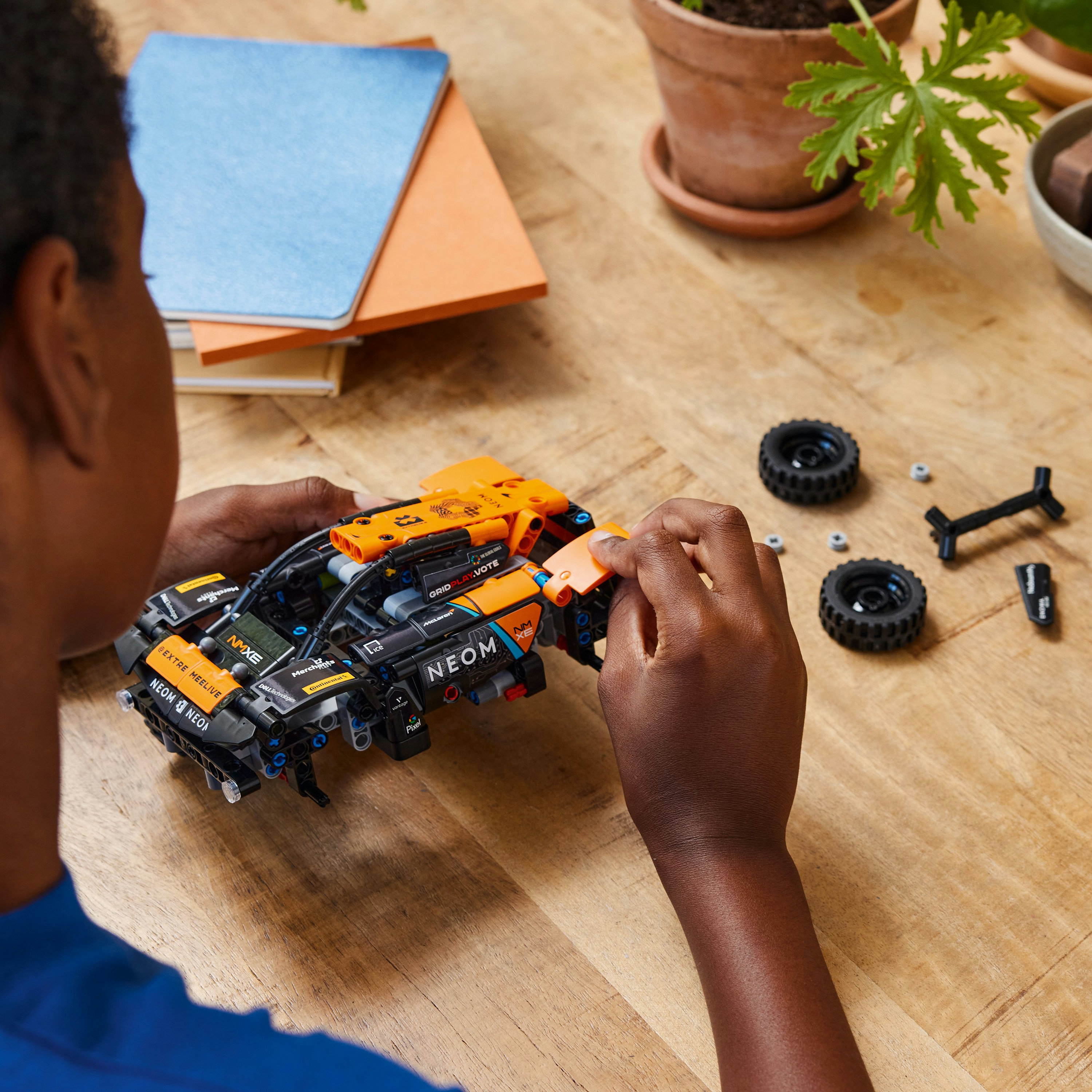 Person baut ein schwarzes und oranges Lego-Auto zusammen. Die Szene ist auf einem Holztisch.