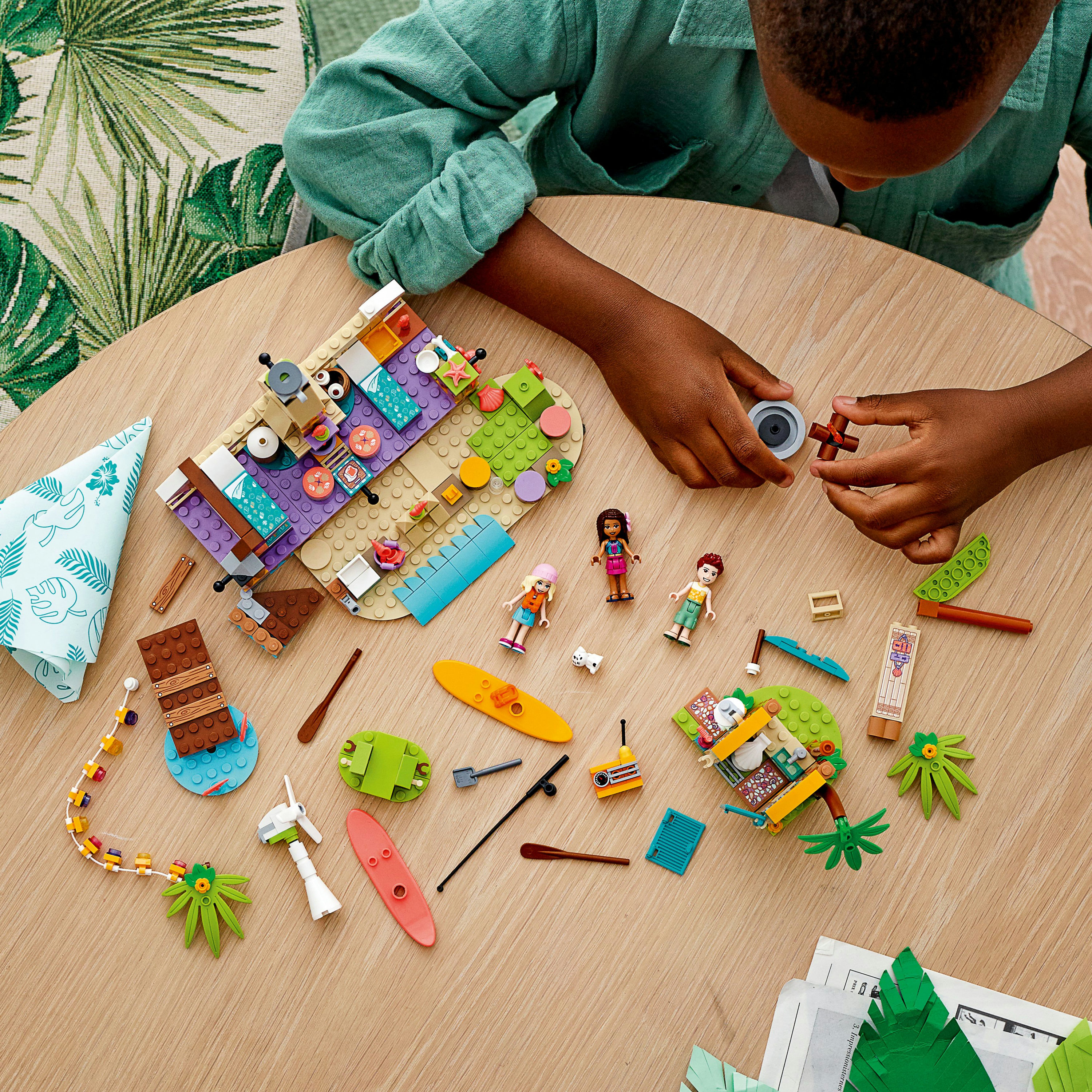 Kind spielt mit einem Lego-Set auf einem Tisch, verschiedene Lego-Teile und Figuren sind sichtbar.