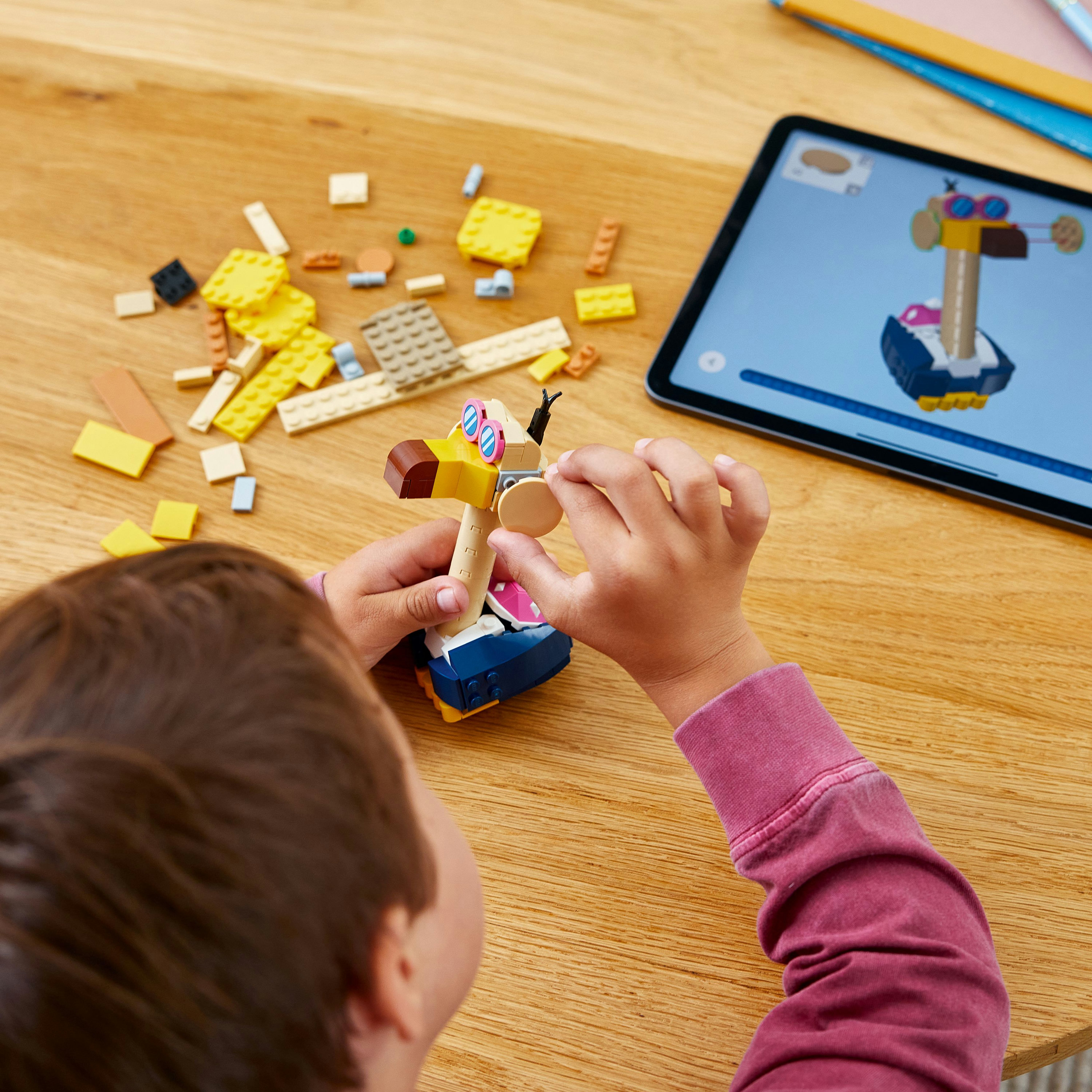 Kind baut ein Lego-Modell eines Vogels, Tablet zeigt Anweisungen.