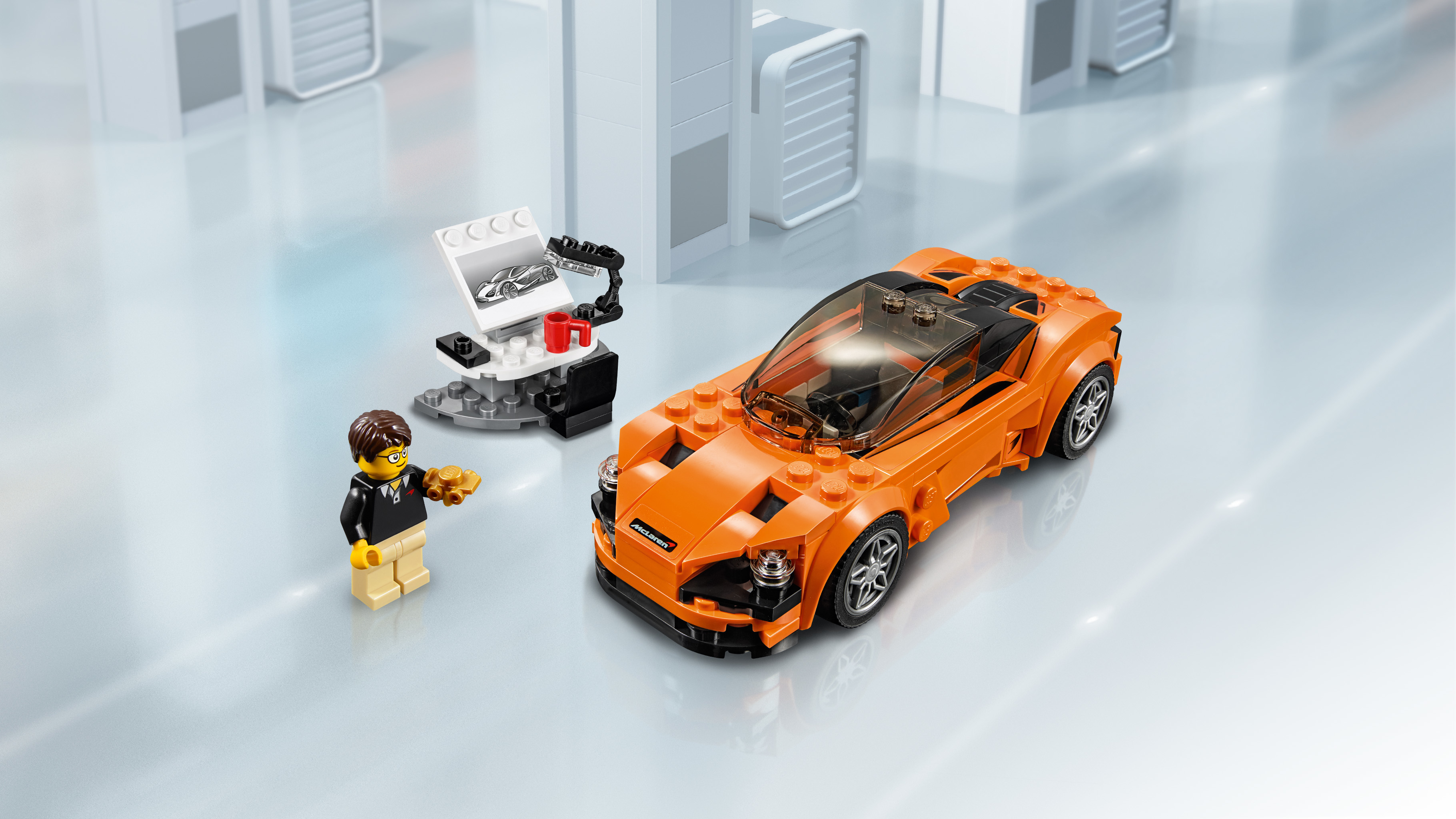 Oranges Lego-Auto und -Figur mit kleiner Werkstatt. Hintergrund ist eine weiße, graue und gläserne Umgebung.