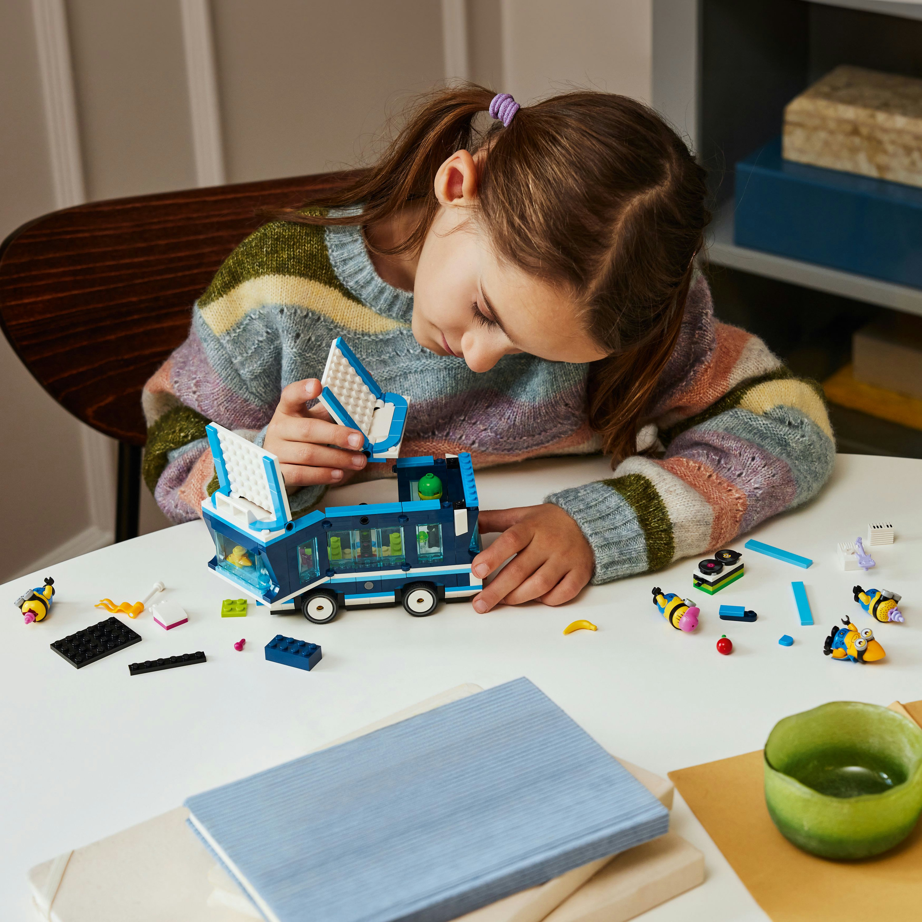 Ein Mädchen baut einen LEGO Friends Bus zusammen, mit Mini-Figuren, einem Tisch und verschiedenen Objekten.