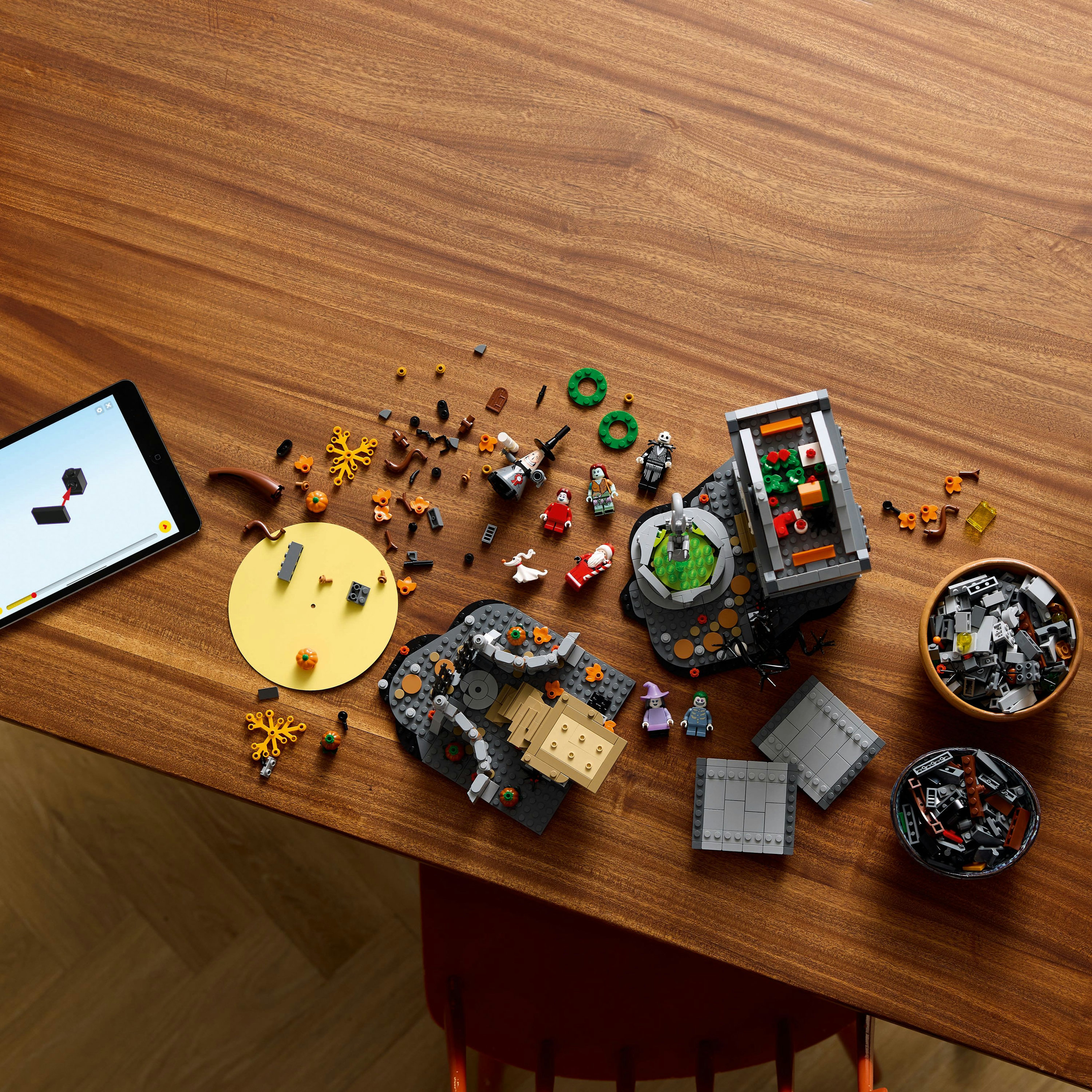 Set Lego sur une table en bois. Comprend divers personnages, citrouilles et structures. Tablette avec instructions.