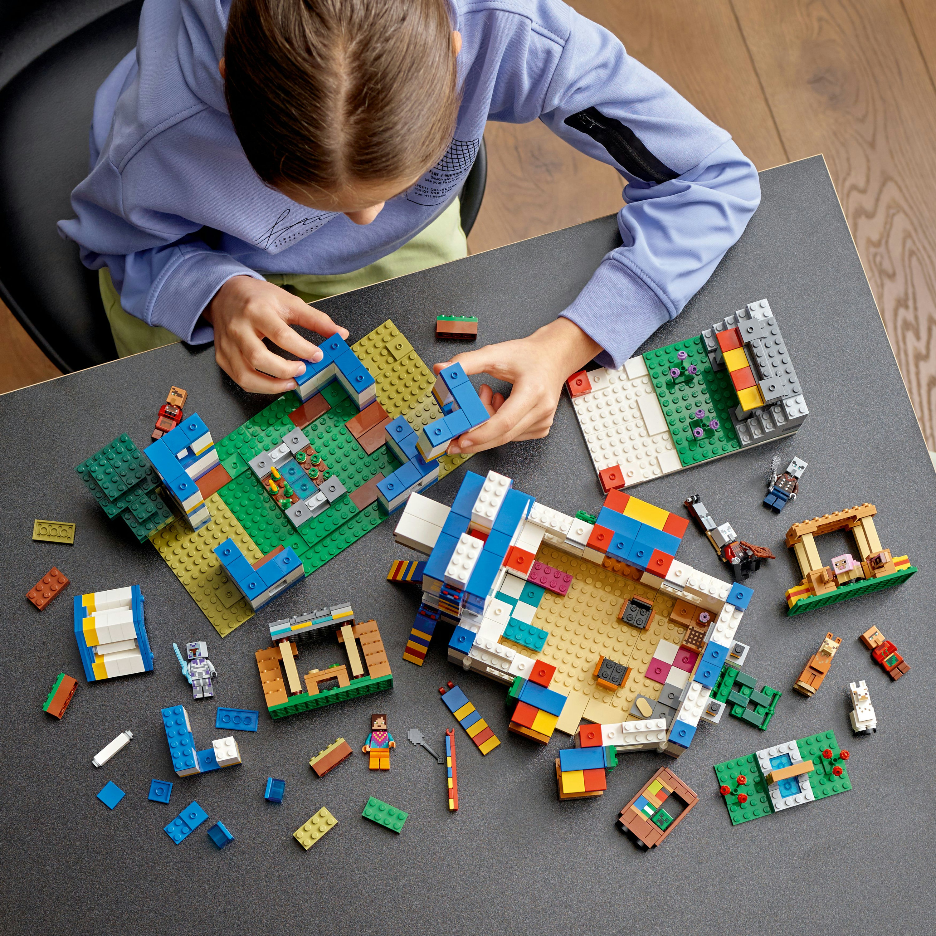 Ein Kind baut eine Lego Minecraft-Szene mit verschiedenen Blöcken und Figuren auf einem schwarzen Tisch zusammen.
