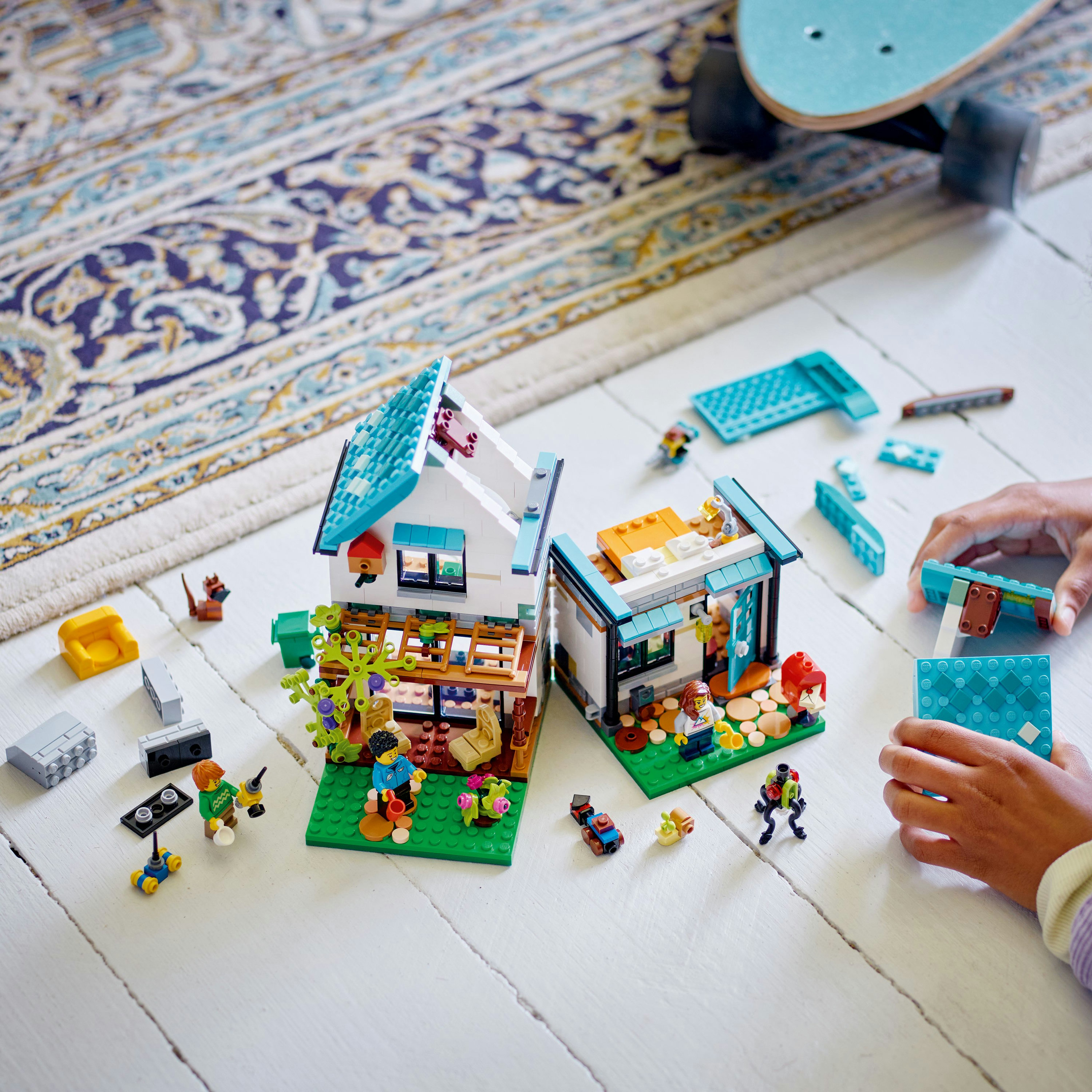 Set Lego: due case in costruzione. Include figure, skateboard e vari mattoncini Lego in un ambiente bianco.