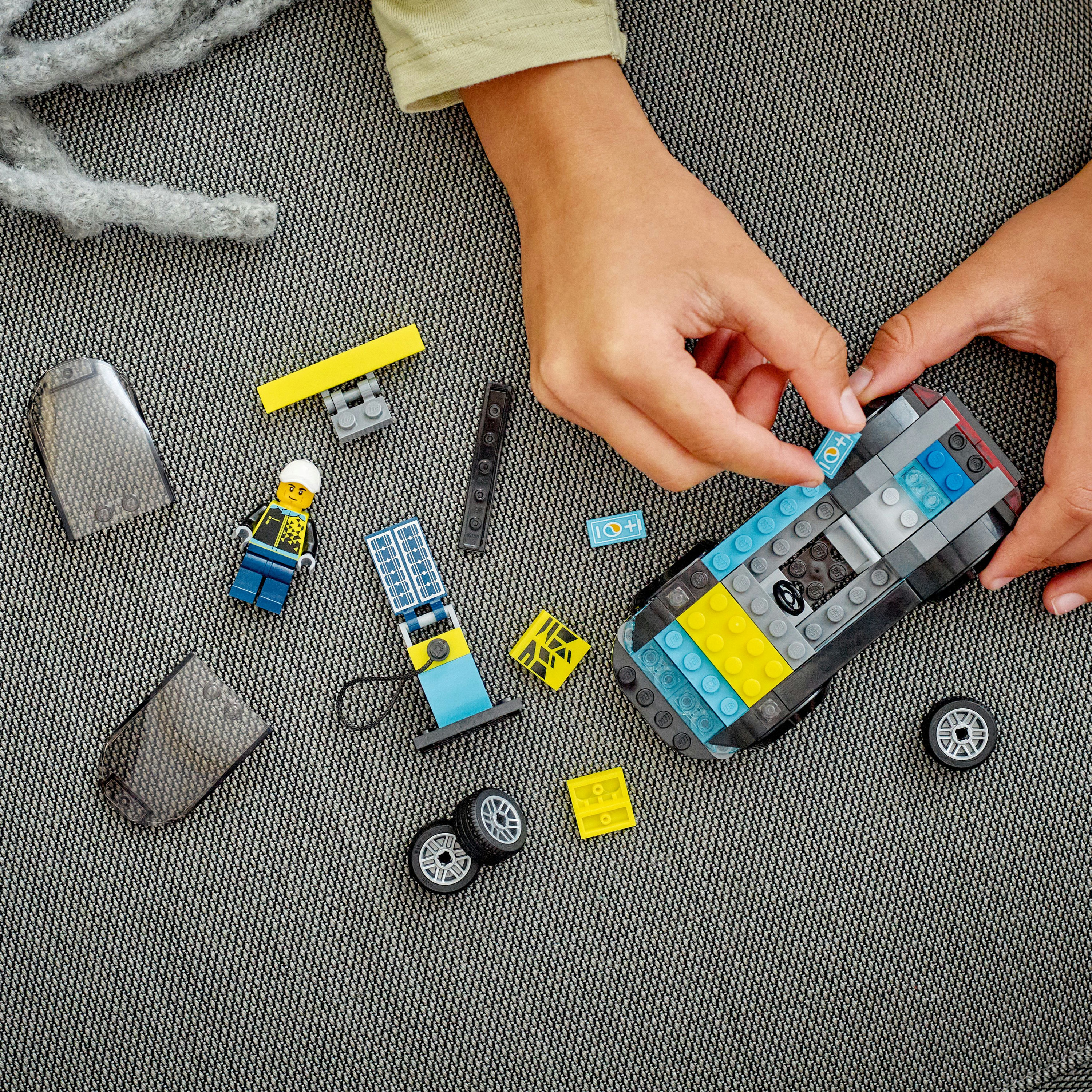 Eller Lego araba yapıyor. Lego parçaları, figürler ve gri bir yüzey içerir.