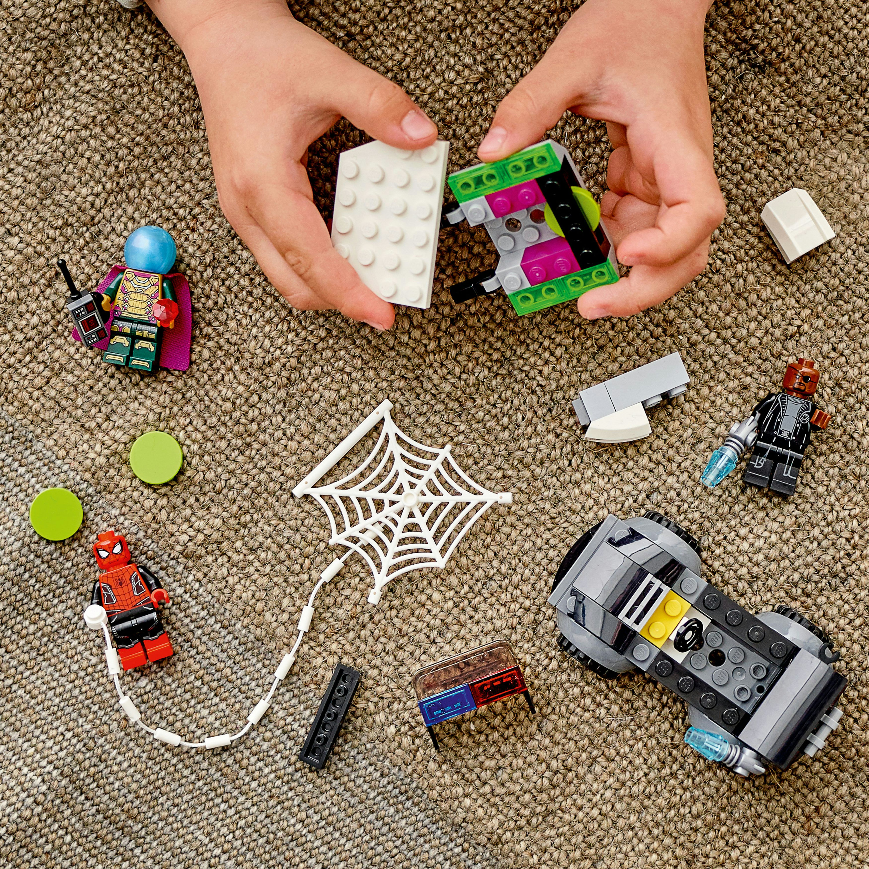 Hände, die Lego-Teile zusammensetzen. Enthält Spider-Man, Green Goblin Minifiguren und ein Netz.