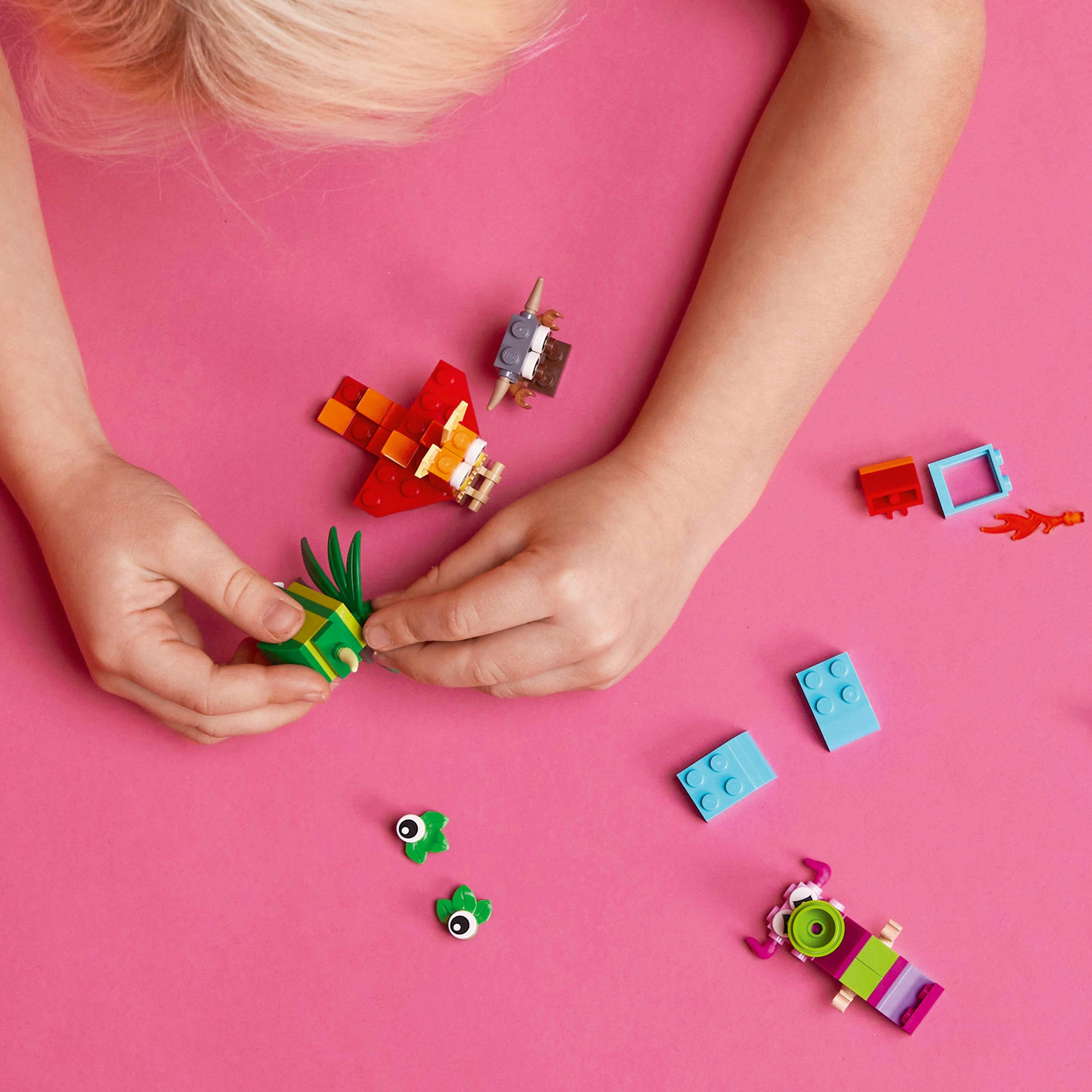 Eller LEGO parçalarıyla inşa ediyor. Pembe arka plan. Çeşitli renkli tuğlalar.