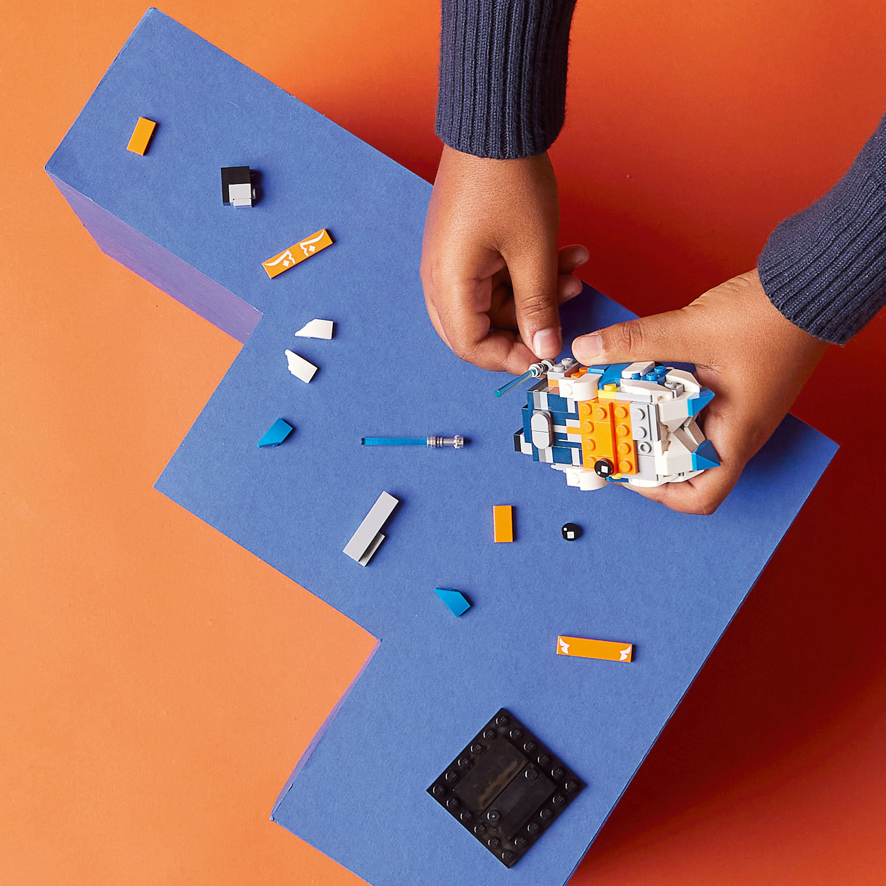 Eine Person baut ein Lego-Raumschiff mit verstreuten Teilen auf blau-orangefarbenem Hintergrund.