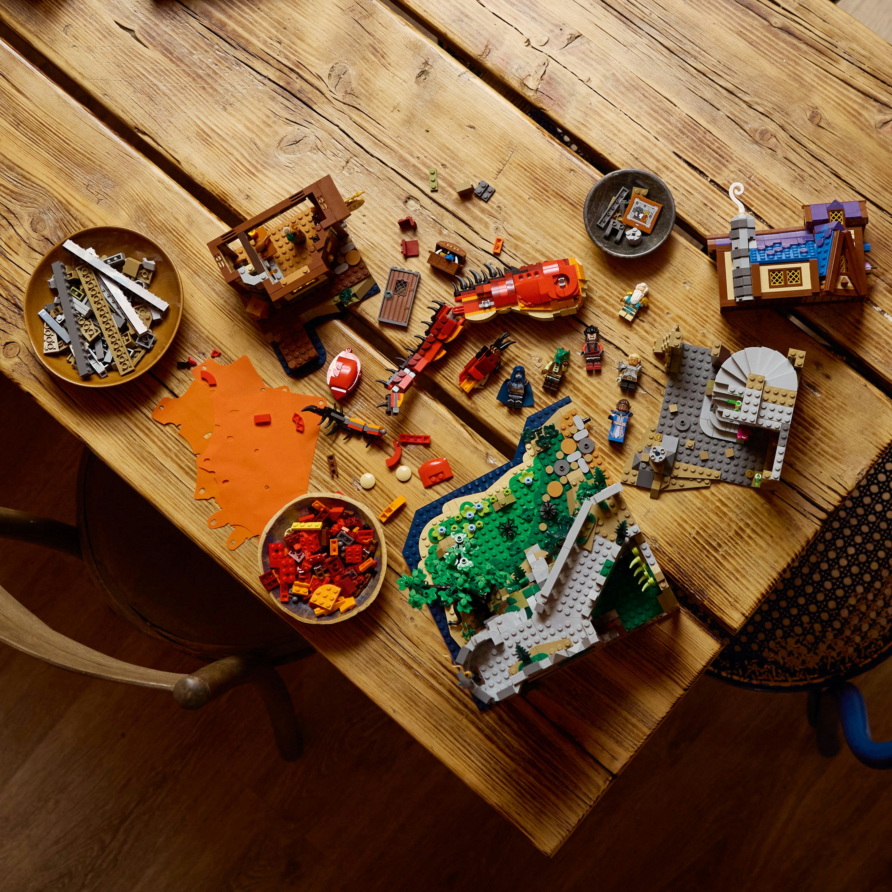 Drewniany stół z klockami Lego. Różne modele Lego w trakcie, wraz z miskami z elementami.