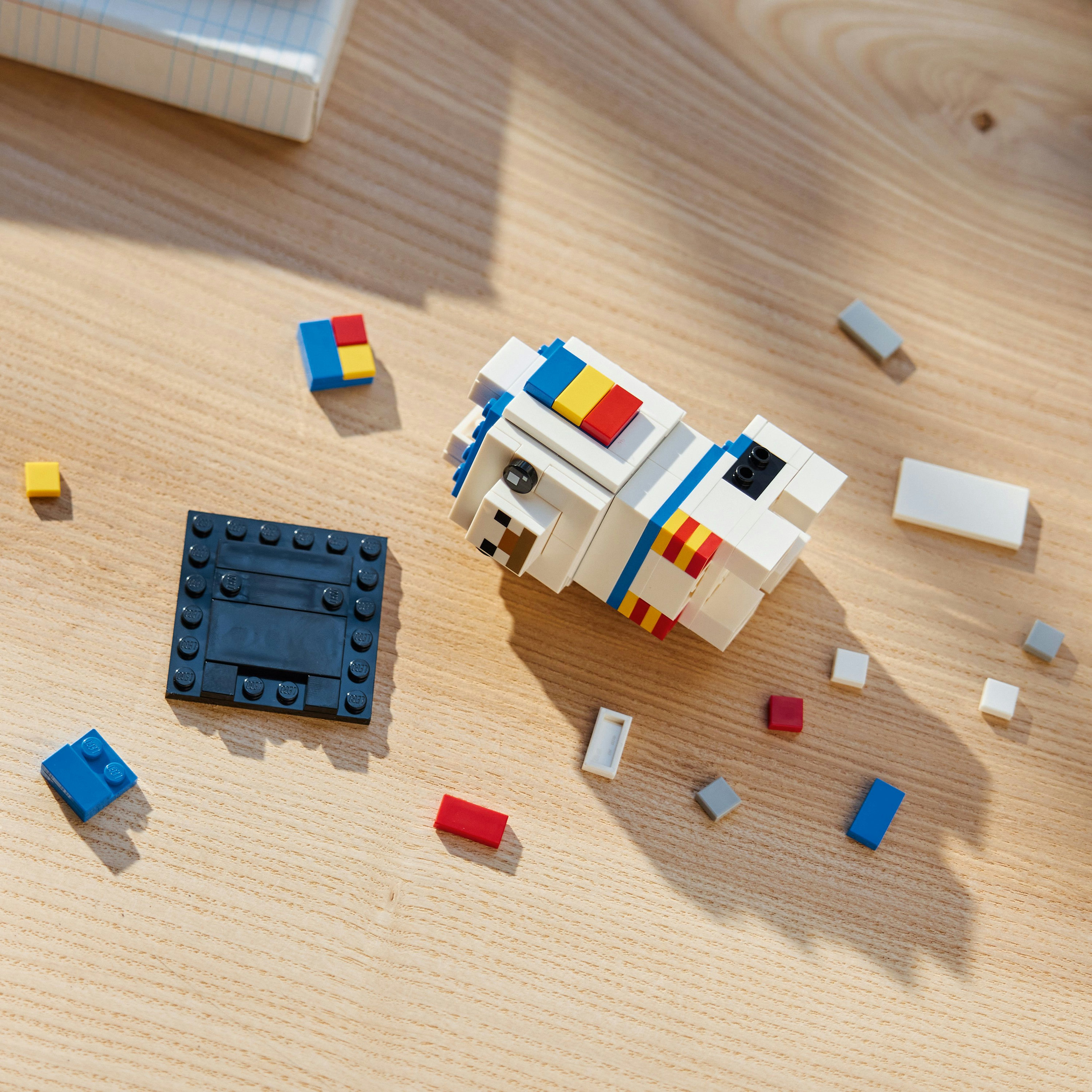 Holztisch mit Lego-Steinen. Enthält einen weißen Hund, eine schwarze Basis und verstreute Steine in verschiedenen Farben.