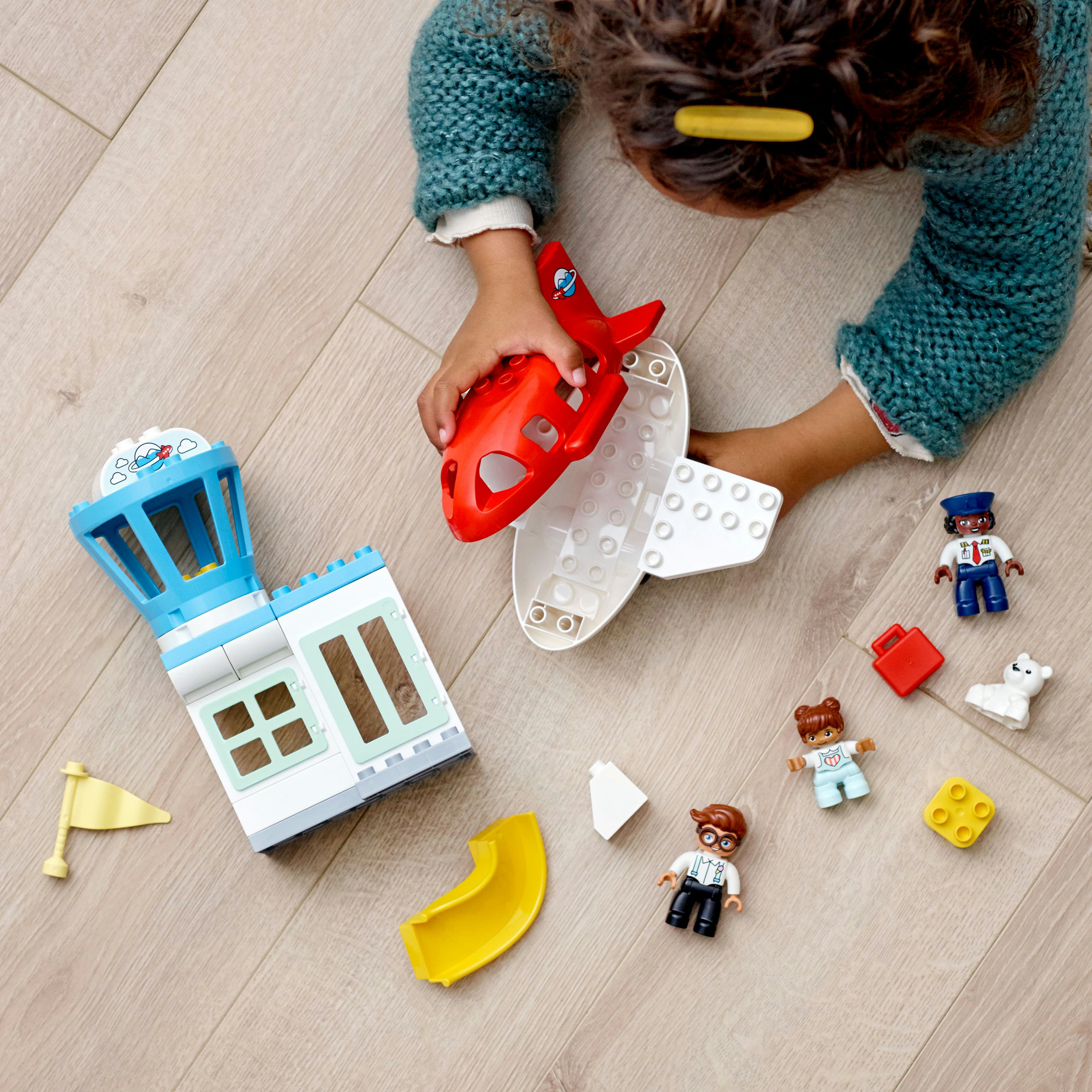 Kind spielt mit Spielzeug-Flughafen-Set, einschließlich Flugzeug, Turm und Figuren. Holzfußboden.
