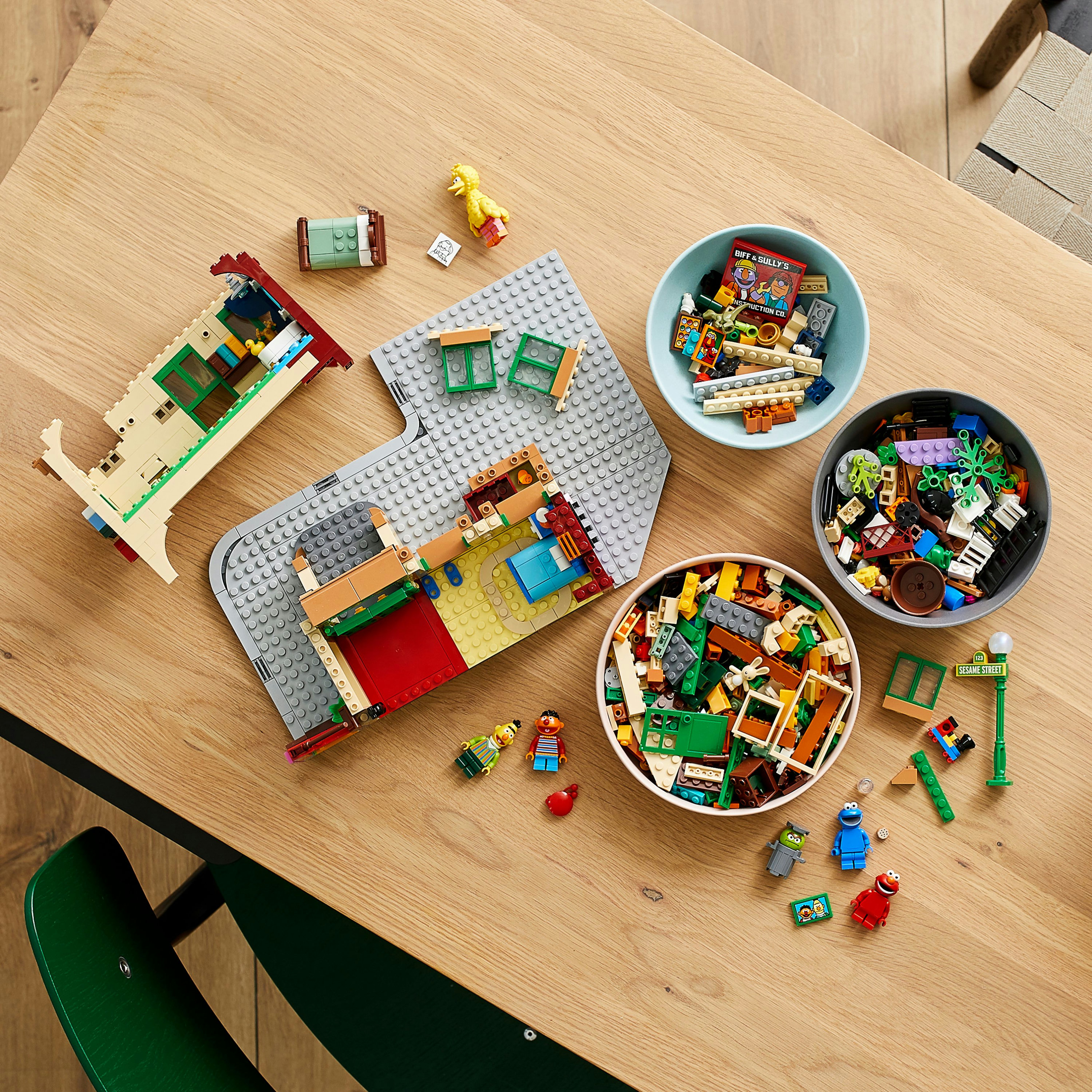Sezioni di edifici Lego Sesame Street disposte su un tavolo. Vengono mostrate anche ciotole di pezzi Lego.