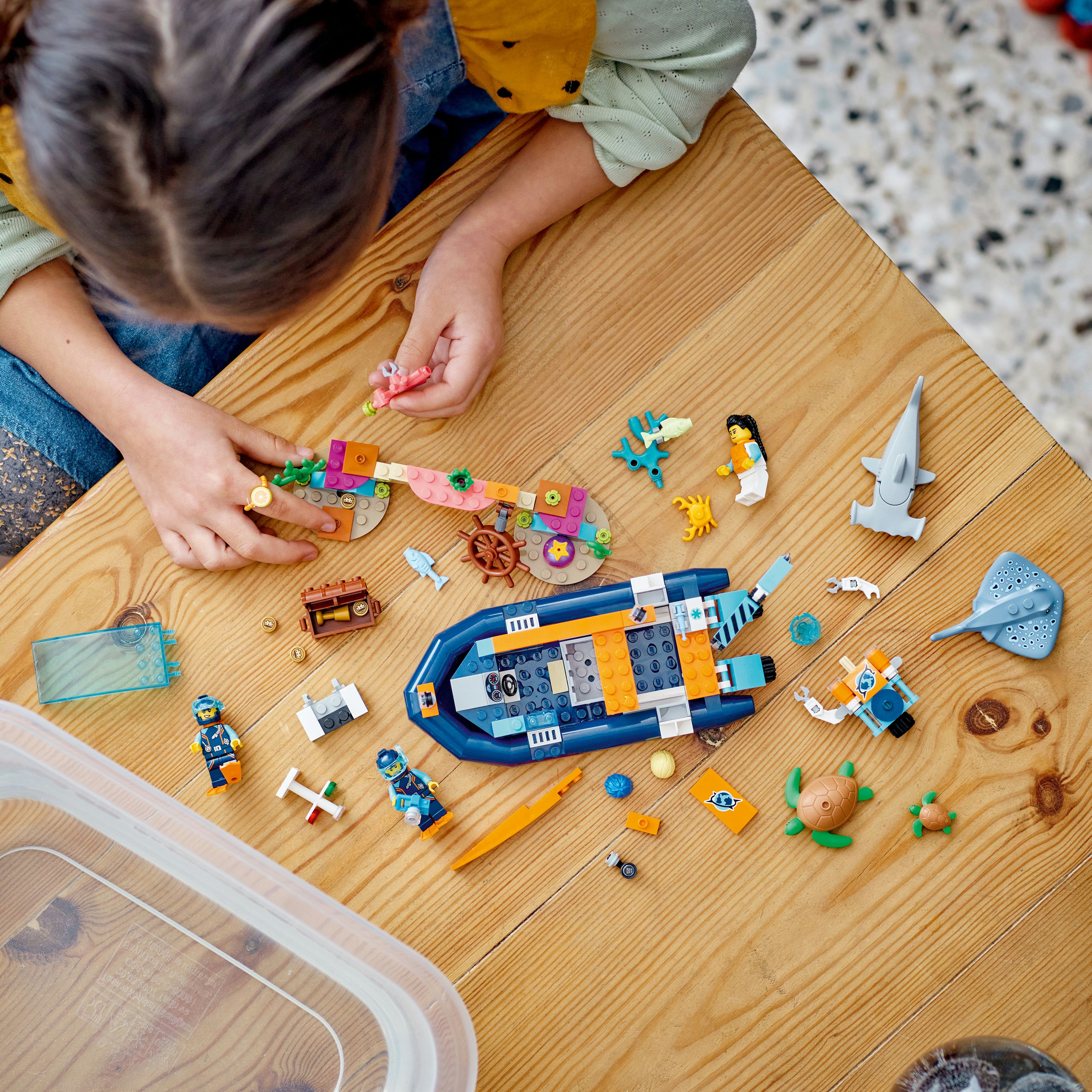 Un bambino gioca con un set Lego di imbarcazioni con una barca, creature marine e figurine su un tavolo di legno.
