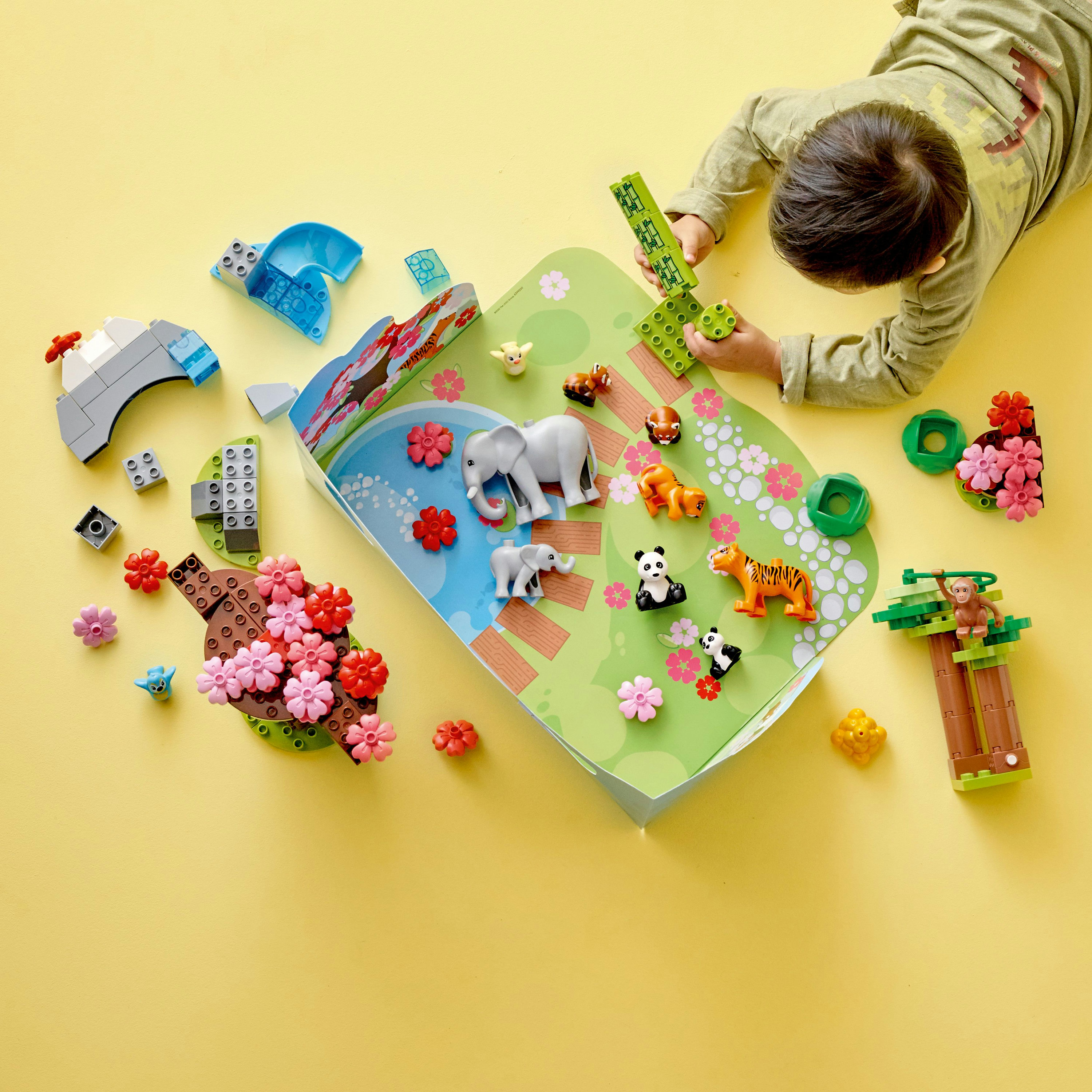 Un niño y un set Lego Duplo con animales de zoológico y una escena de parque sobre una superficie amarilla.