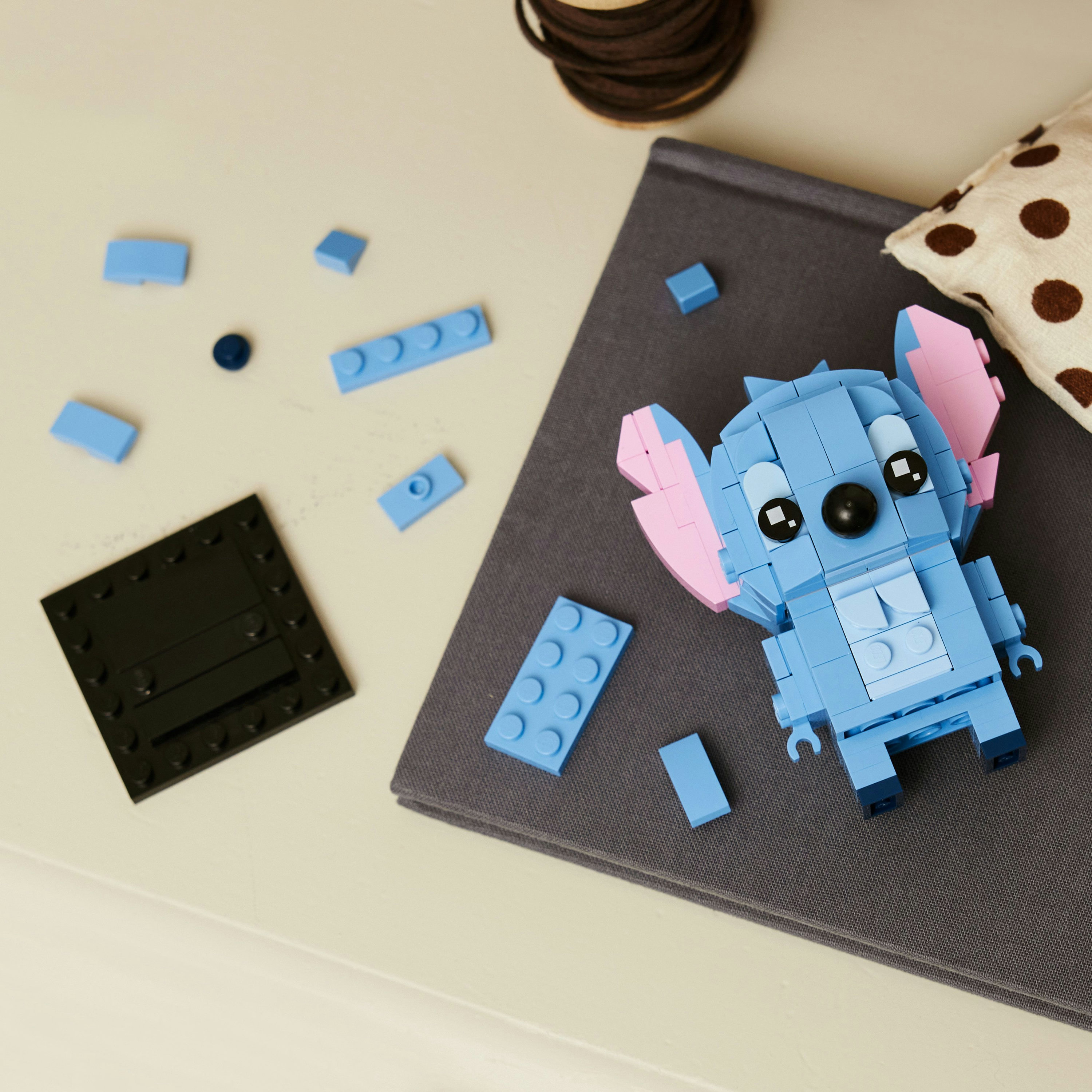 Gri bir yüzey üzerinde inşa edilen Lego Stitch modeli, etrafa dağılmış mavi Lego parçalarıyla.