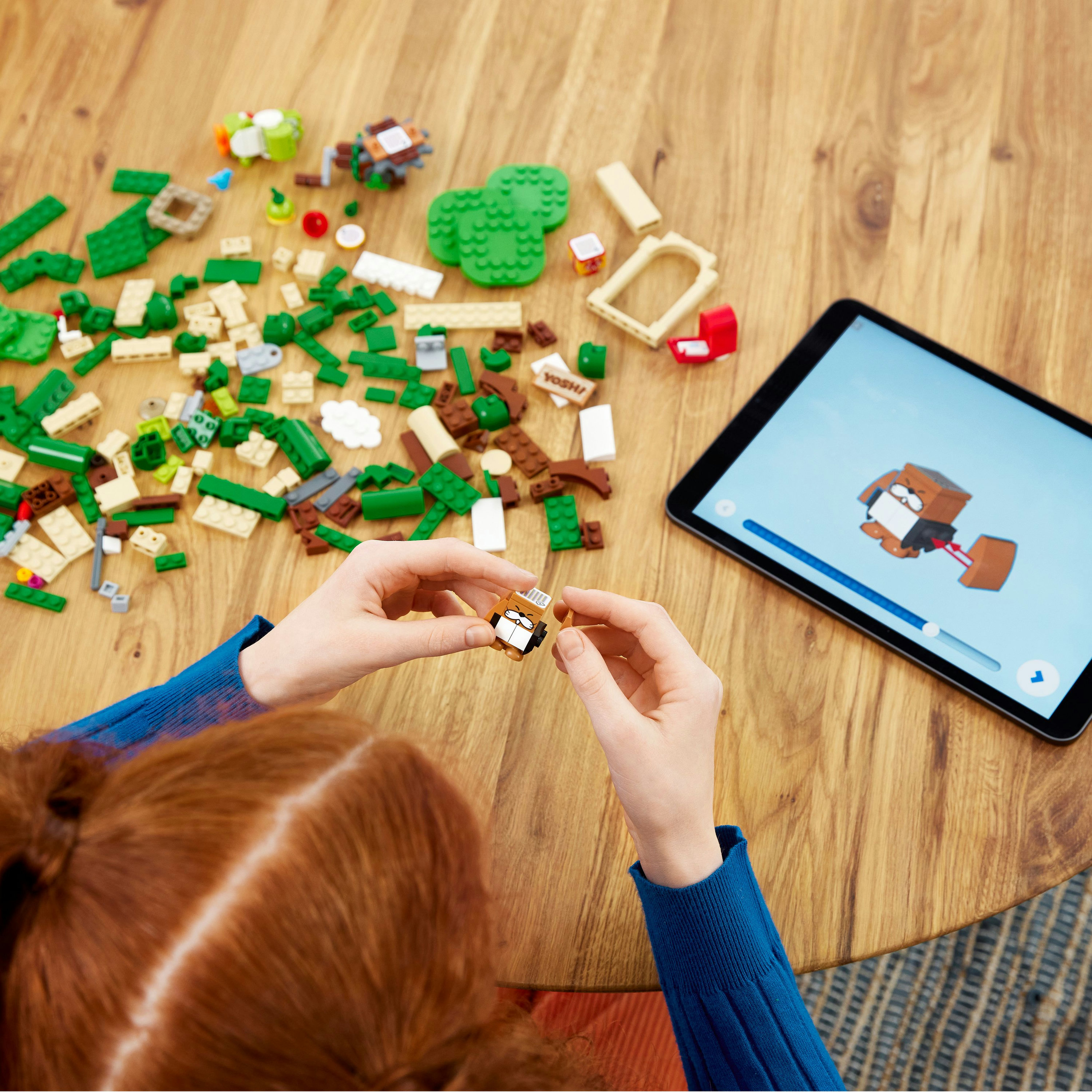 Handen die een Lego figuur in elkaar zetten, naast Lego stenen en een tablet met instructies.