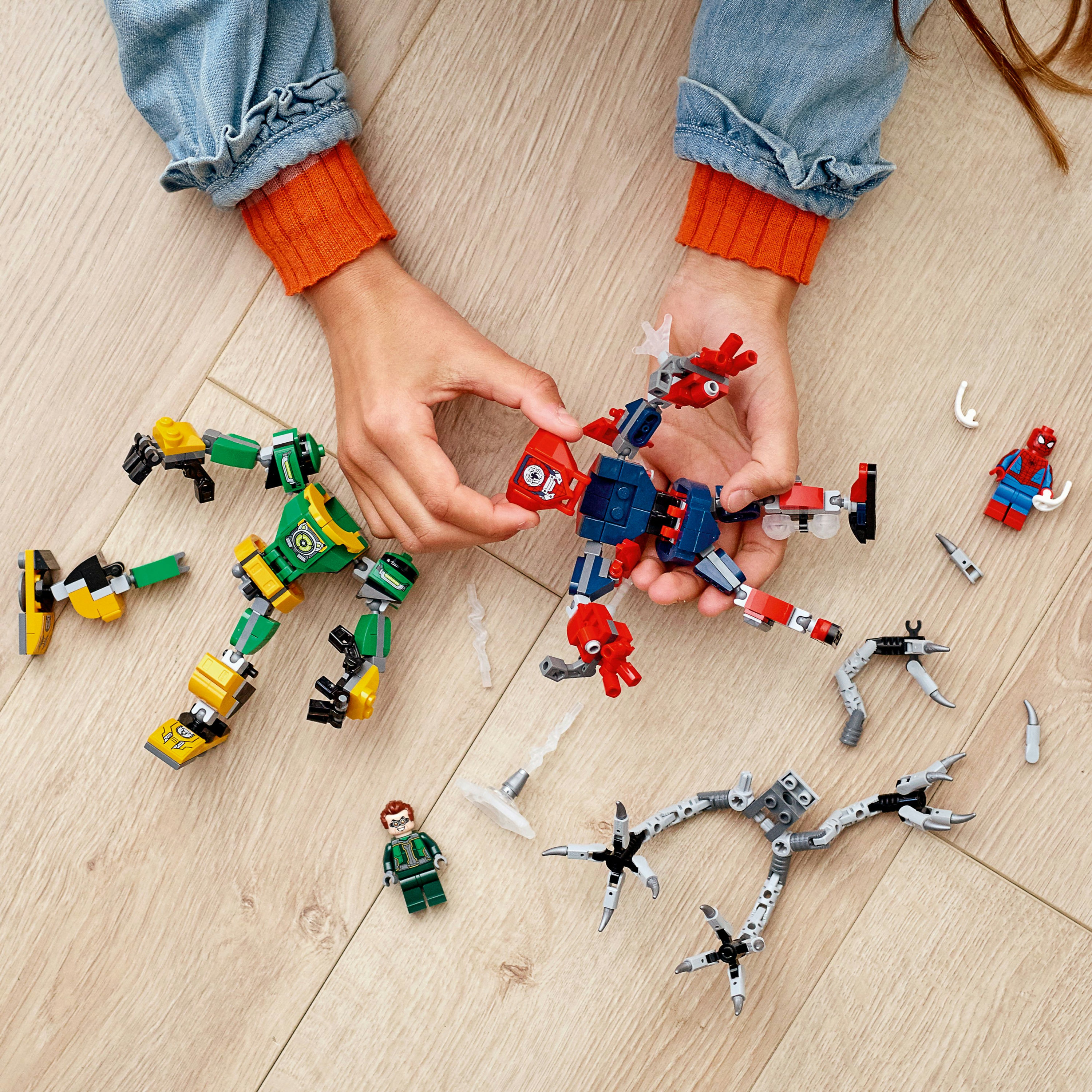 A child is playing with Lego superhero figures. There are two robots and a Spiderman figure.