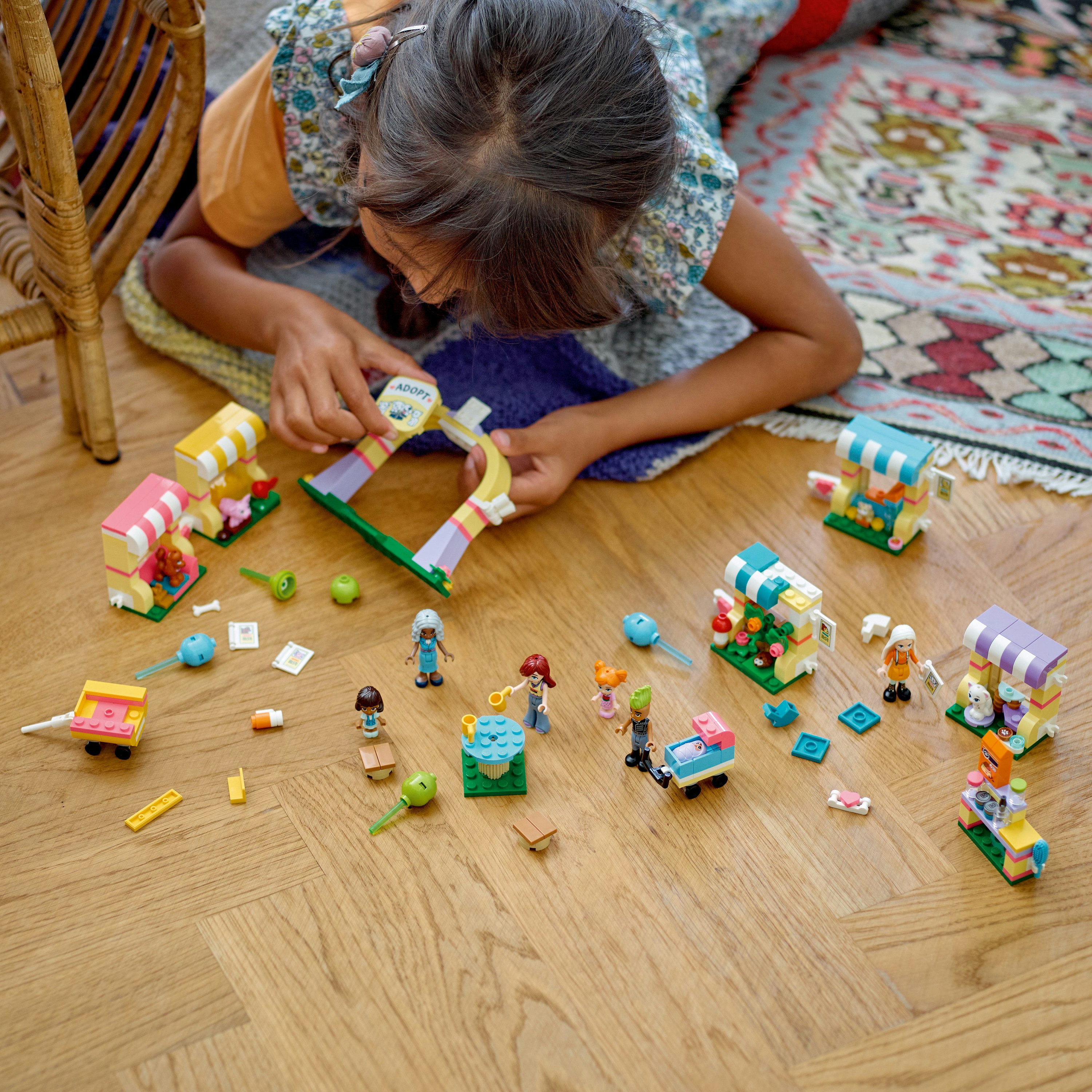 Una ragazza gioca con un set LEGO Friends, una scena di mercato con varie bancarelle e figure.
